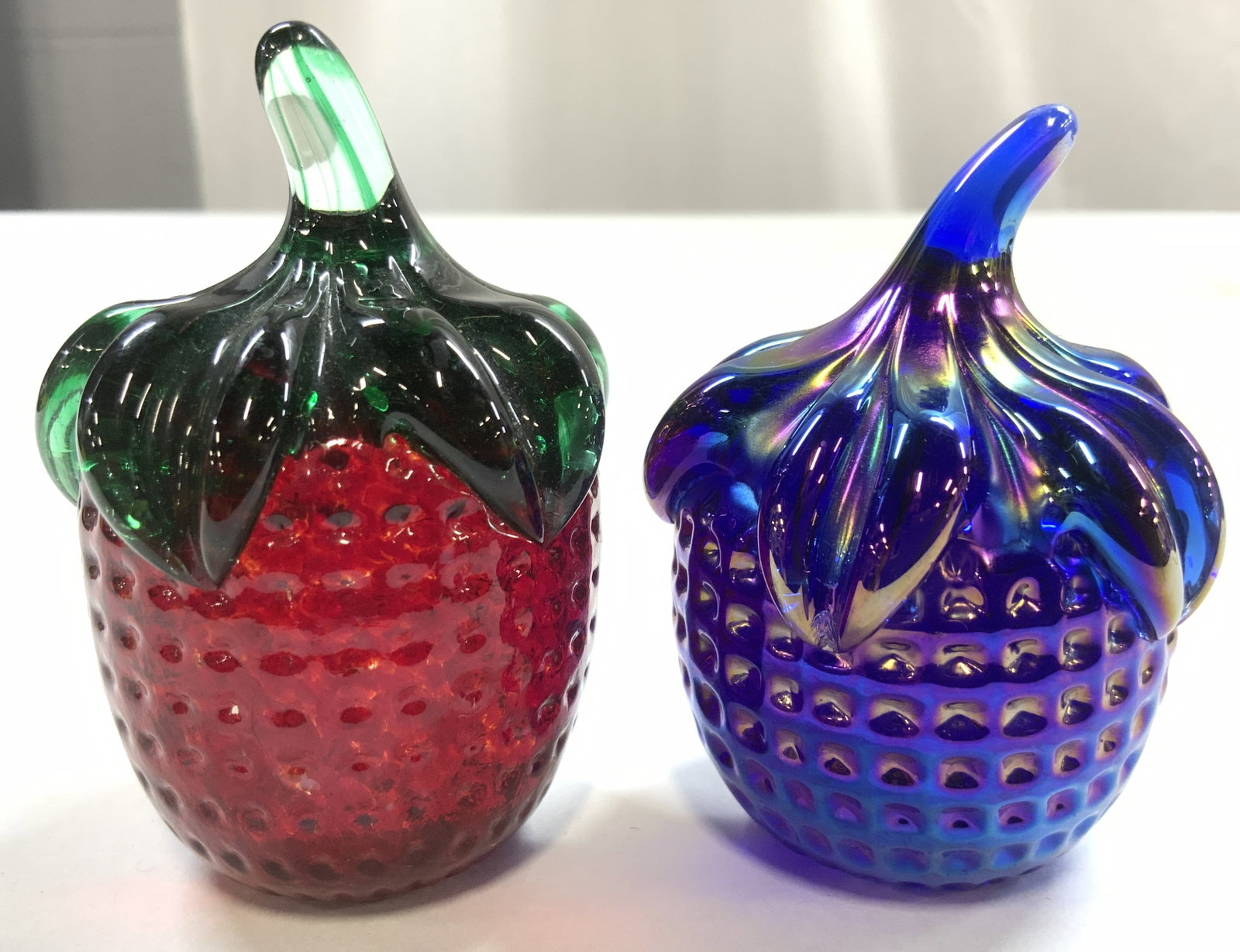 GIBSON Art Glass Iridescent Glass Strawberries: Undersides reads GIBSON. Lot includes 1 art glass (green and red toned) & 1 iridescent Art glass strawberry (blue, purple, green iridescent luster. Slightly larger strawberry measures approximately 3 