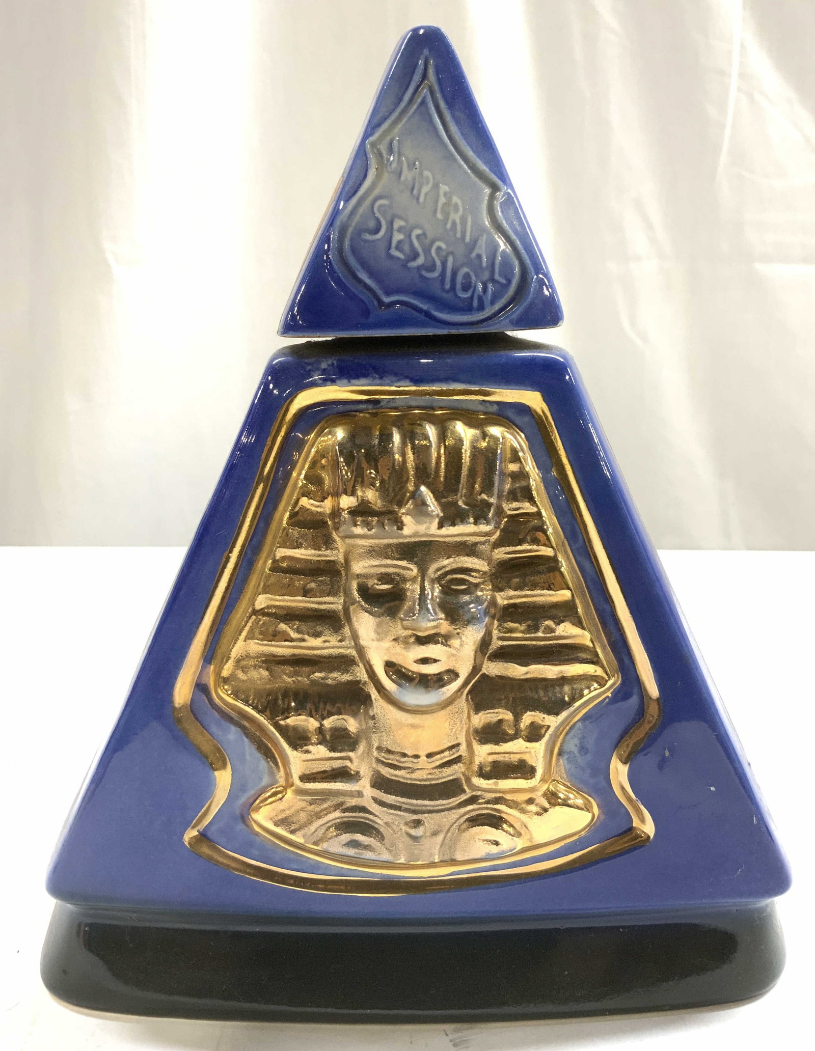 JIM BEAM Imperial Session Pyramid Ceramic Decanter: Decanter is JIM BEAM. Piece is vintage and ceramic. Decanter includes stamp. Backside reads INDIANA. Piece is blue with gilt Egyptian head detail. Piece includes lid. Decanter measures approximately 8