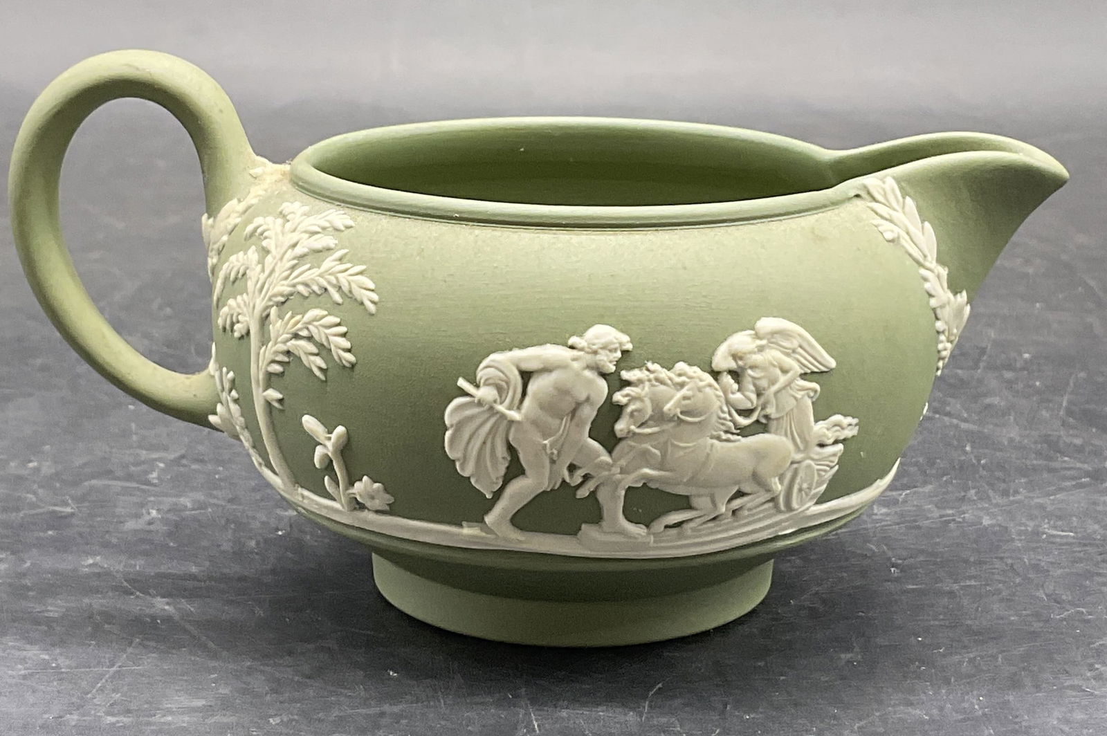 WEDGWOOD ENGLAND Green Jasperware Creamer: Vintage WEDGWOOD ENGLAND Green Jasperware Creamer. Underside signed WEDGWOOD MADE IN ENGLAND, verbiage is worn. Raised Greco Roman motif along the sides. Measures approx. 2.5H x 5W in. Measurement inc