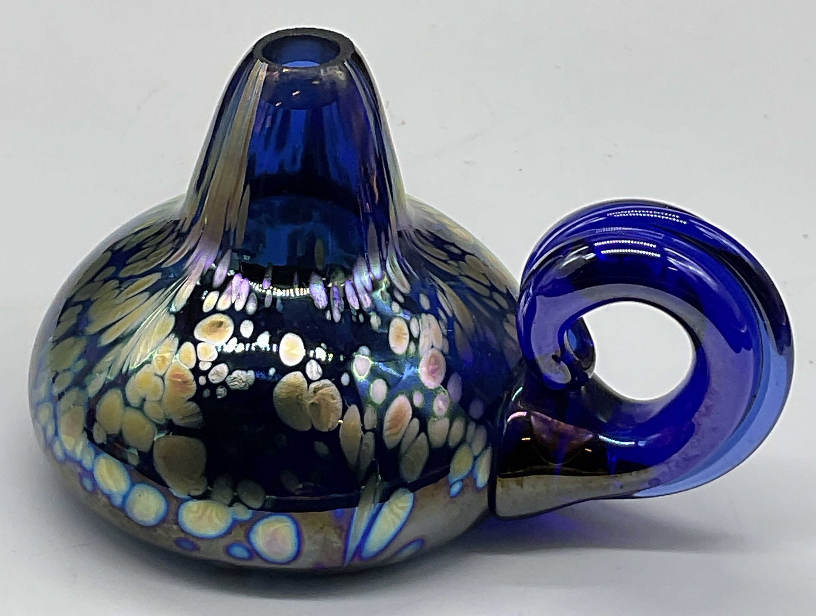 1988 FISKE Artist Signed Art Glass Finger Oil Lamp: Fiske iridescent blue art glass finger oil lamp. Measures approx. 2.75H x 3.75W in. Underside signed FISKE 88. Surface wear consistent with age, use, and exposure. Pitting to glass. home decor, home a