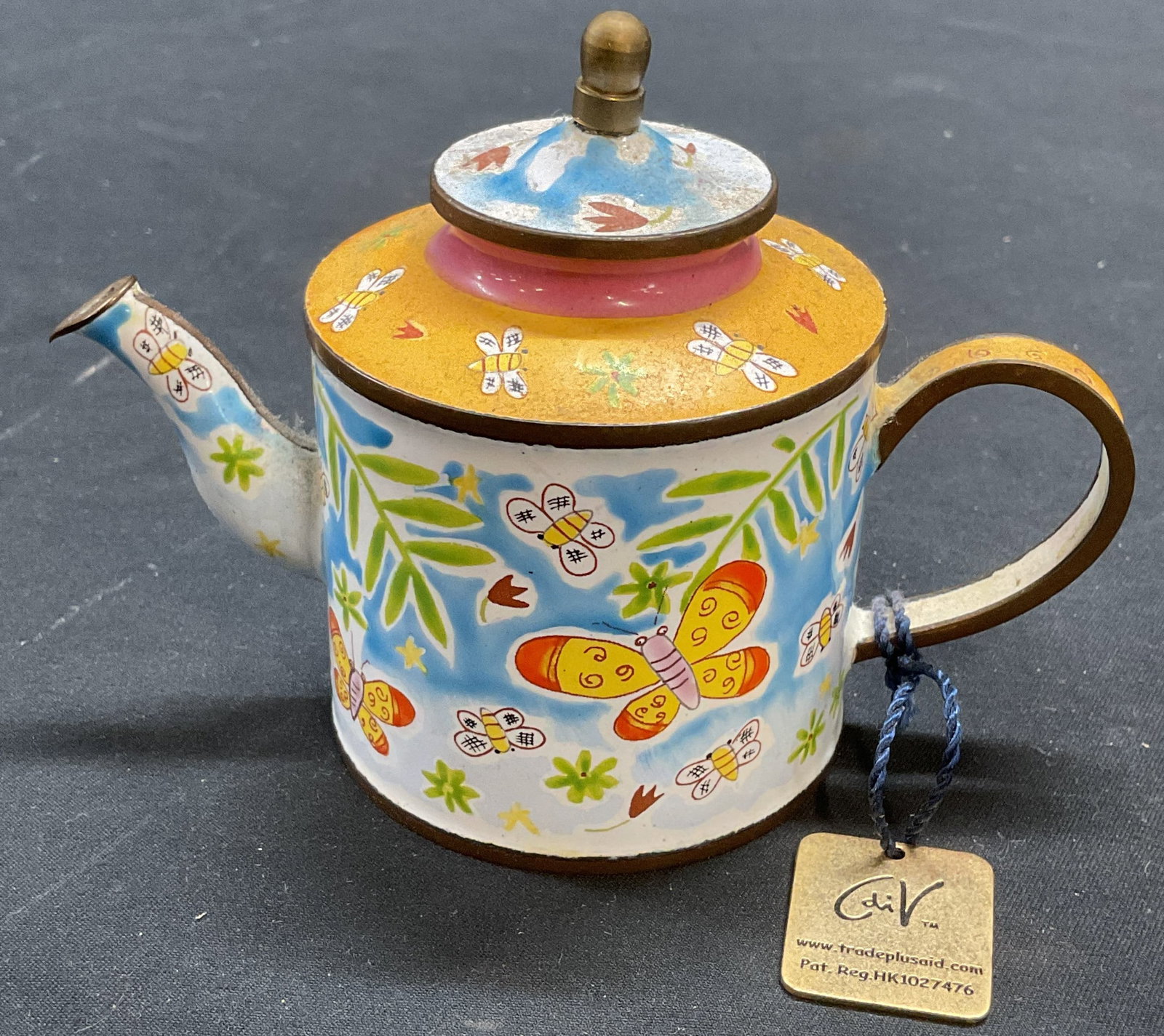2003 Trade Plus Aid Enamel Teapot Figural: 2003 limited edition Trade Plus Aid teapot figural. Enameled brass with butterfly design. Designed by C Madicott. Edition number 574. Signed on underside. Measures approx 5 x 2.25 x 3.5 inches. Some w
