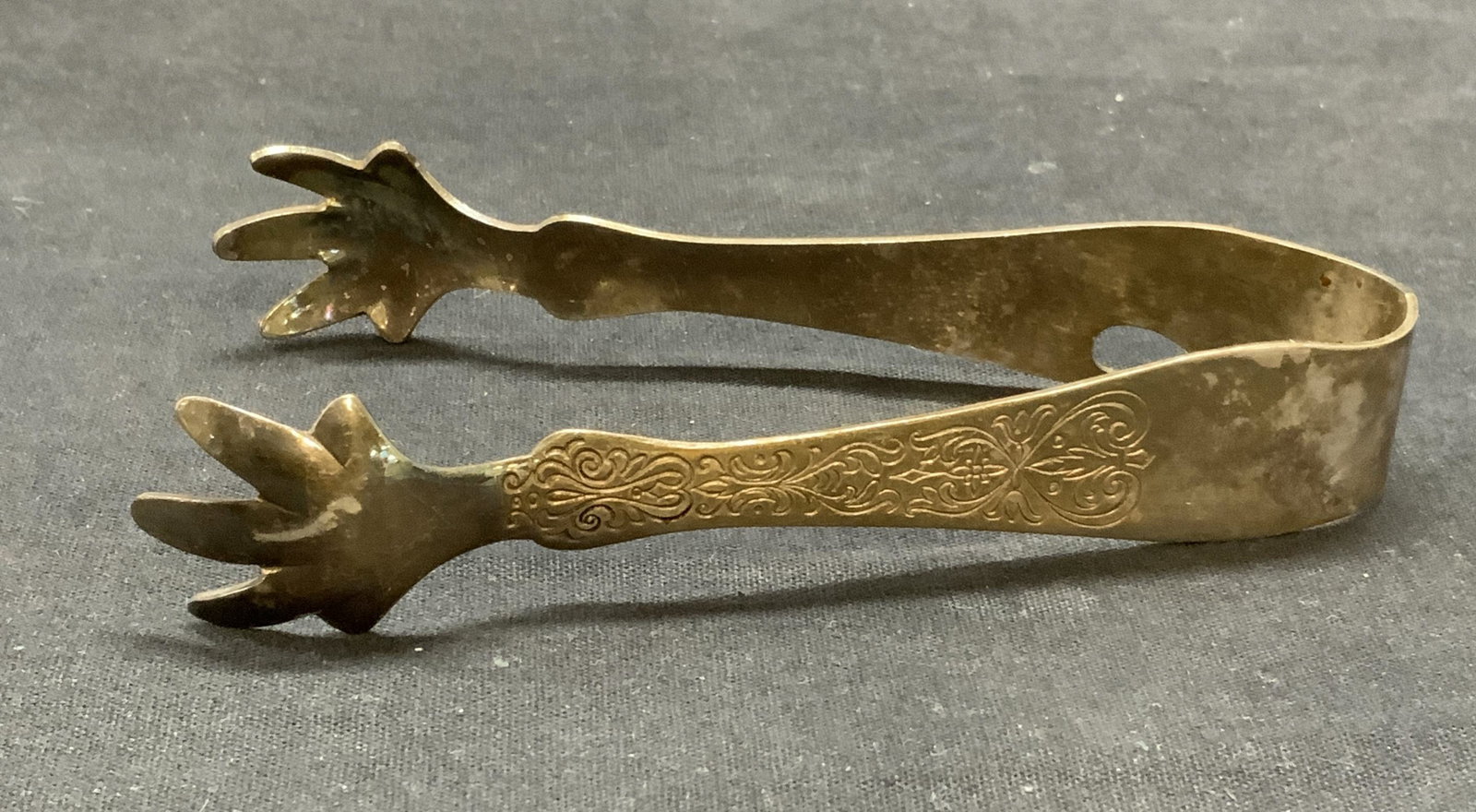 Vintage Silver Plated Claw Tongs: Vintage silver plated tongs with claw motif and etched scroll detail. Measures approx. 5 inches long, 2.25 inches wide. Some surface wear including scratching and patina observed. Tongs, vintage tongs