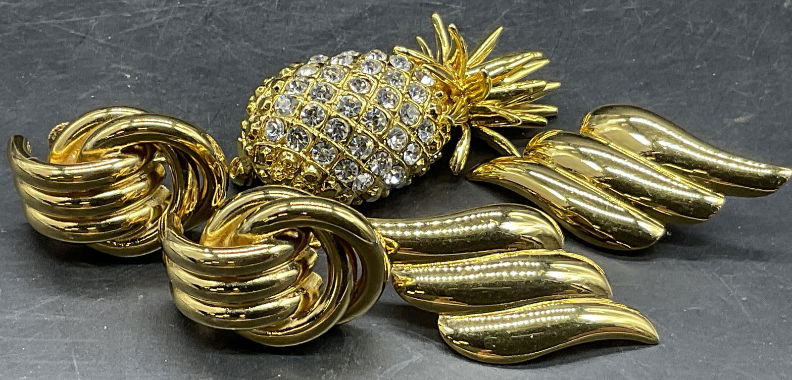 Lot 3 NAPIER, MONET + Gold Tone Metal Jewelry: A pair of Monet clip on earrings, a pair of Napier screw back earrings, and a bejeweled pineapple brooch. All pieces are crafted from gold tone metal. Pineapple brooch measures approx. 1.75L x .75W in