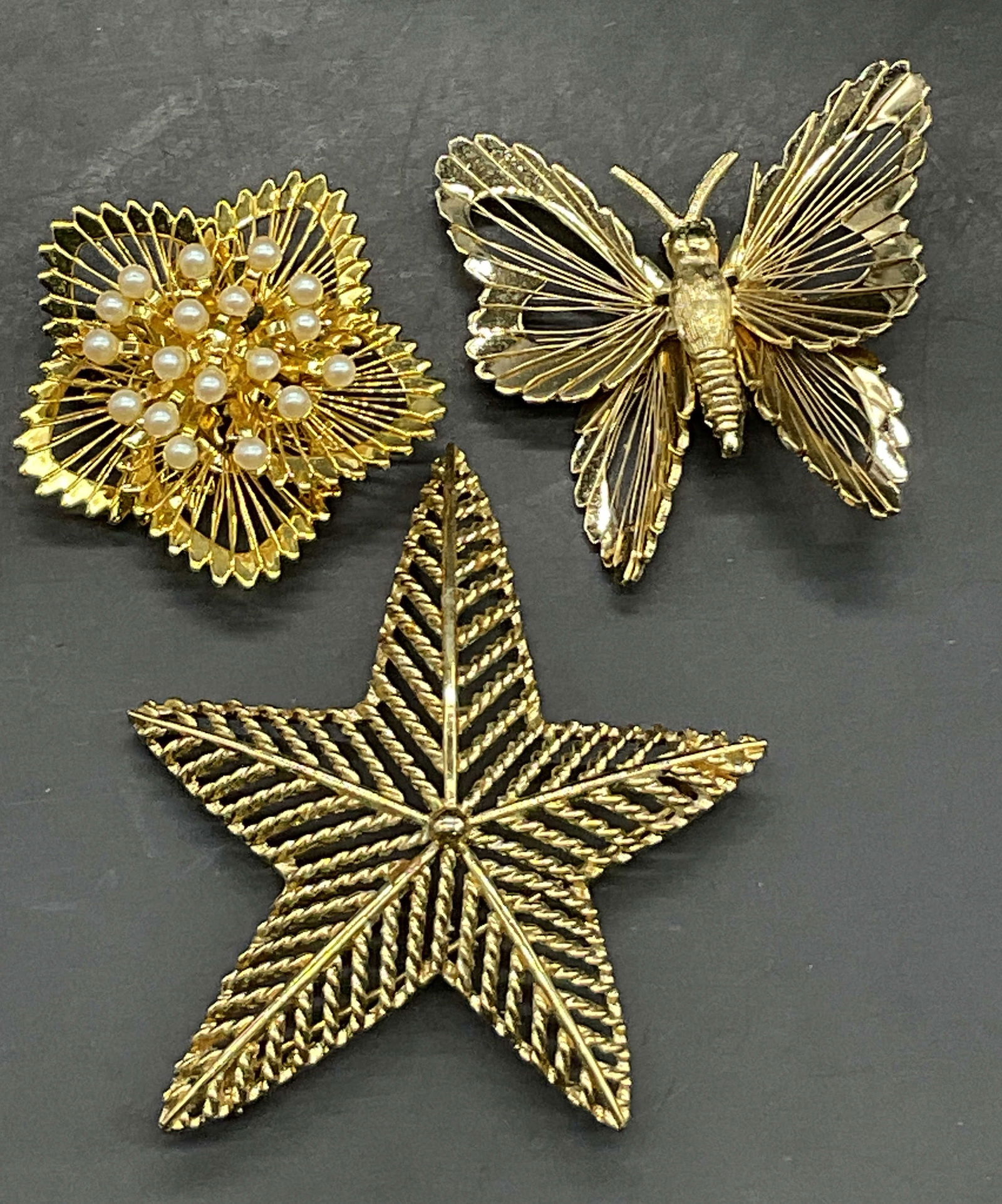 Lot 3 MONET Signed Vintage Brooches, Butterfly +: Three MONET Signed Vintage Brooches. Crafted from gold tone metal and signed MONET to the reverse. Includes a butterfly, a star, and a floral form with a pearlescent cluster. Metal pin backings to the