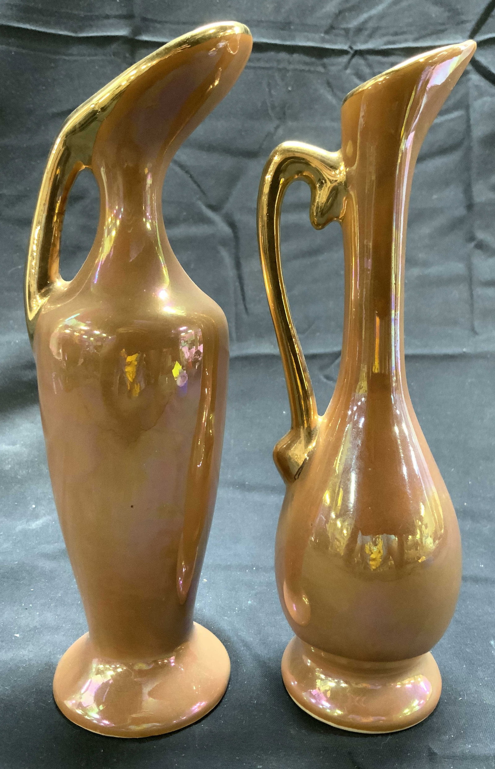 Lot 2 Assorted Porcelain Ewers W Gilt Rims: Lot includes 2 Ewers. Each are peach toned with iridescent lusters. Pieces each have gilt handles and rims. Ewers are each footed. Slightly larger piece measures approximately 7.25 inches tall 2.25 in