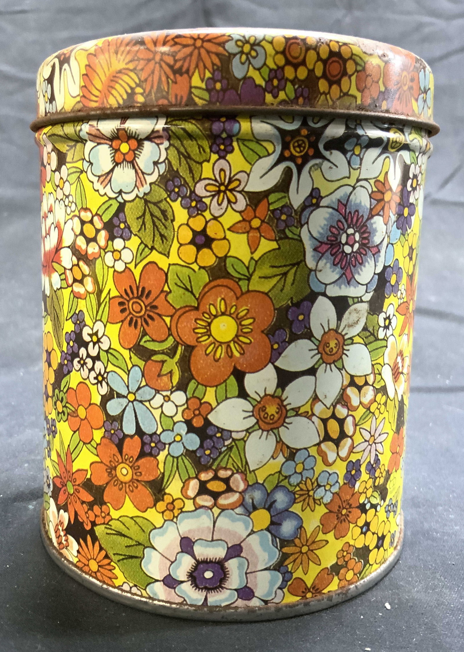 Vintage Floral Detailed Tin W Lid: Tin is vintage. Piece has intricate multi toned floral and leaf detail. Tin includes lid. Piece has cylindrical form. Tin measures approximately 4.25 inches tall 3.5 inches wide. Tin, floral tin, Vint