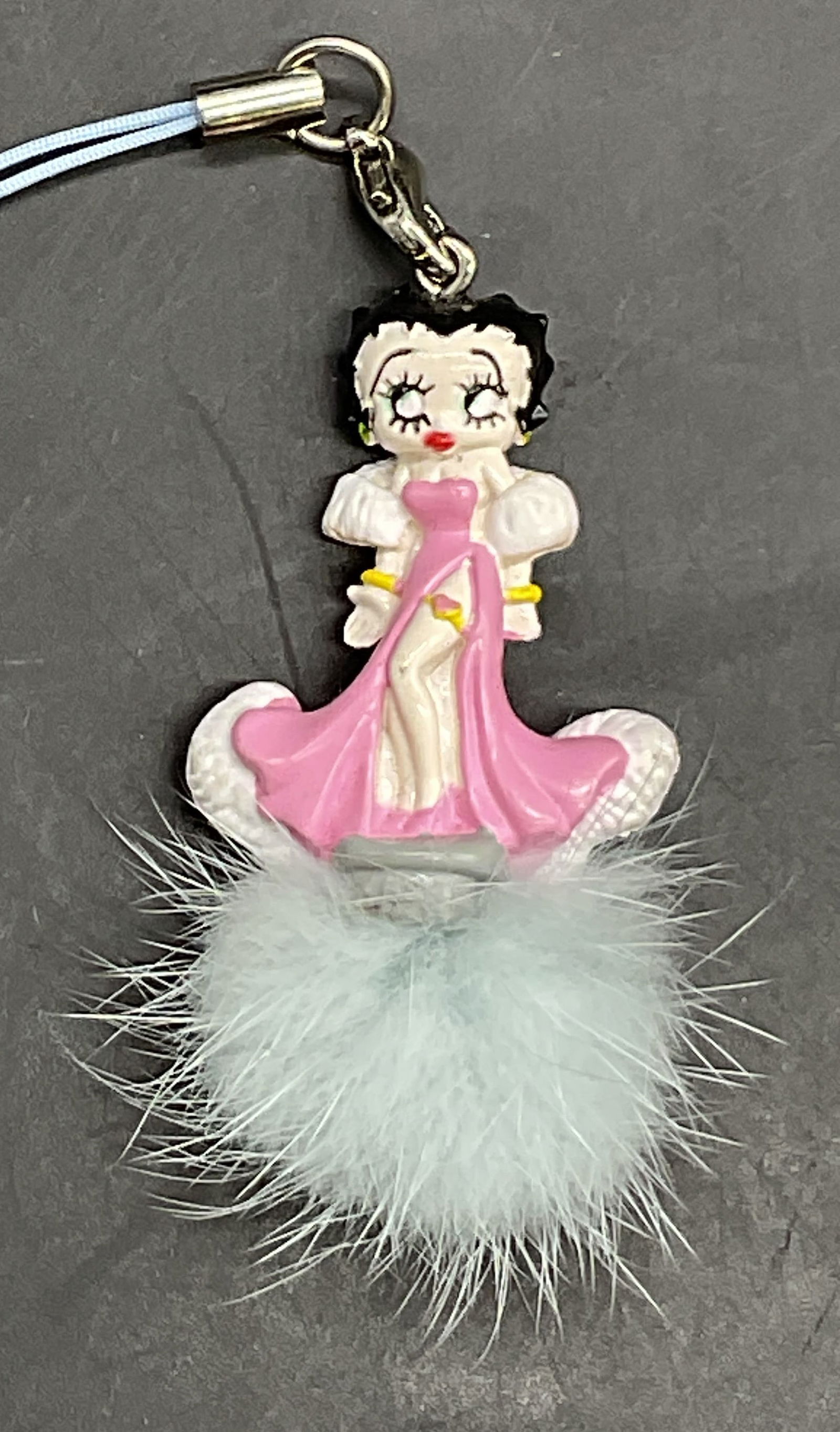 Betty Boop Figural Fuzzy Keychain: Betty Boop Figural Fuzzy Keychain. Betty Boop is depicted wearing a pink robe. Beneath her is a fuzzy blue tuft. Bail to the top of her head with blue cord. Measures approx. 4.5L x 1W in. Measurement