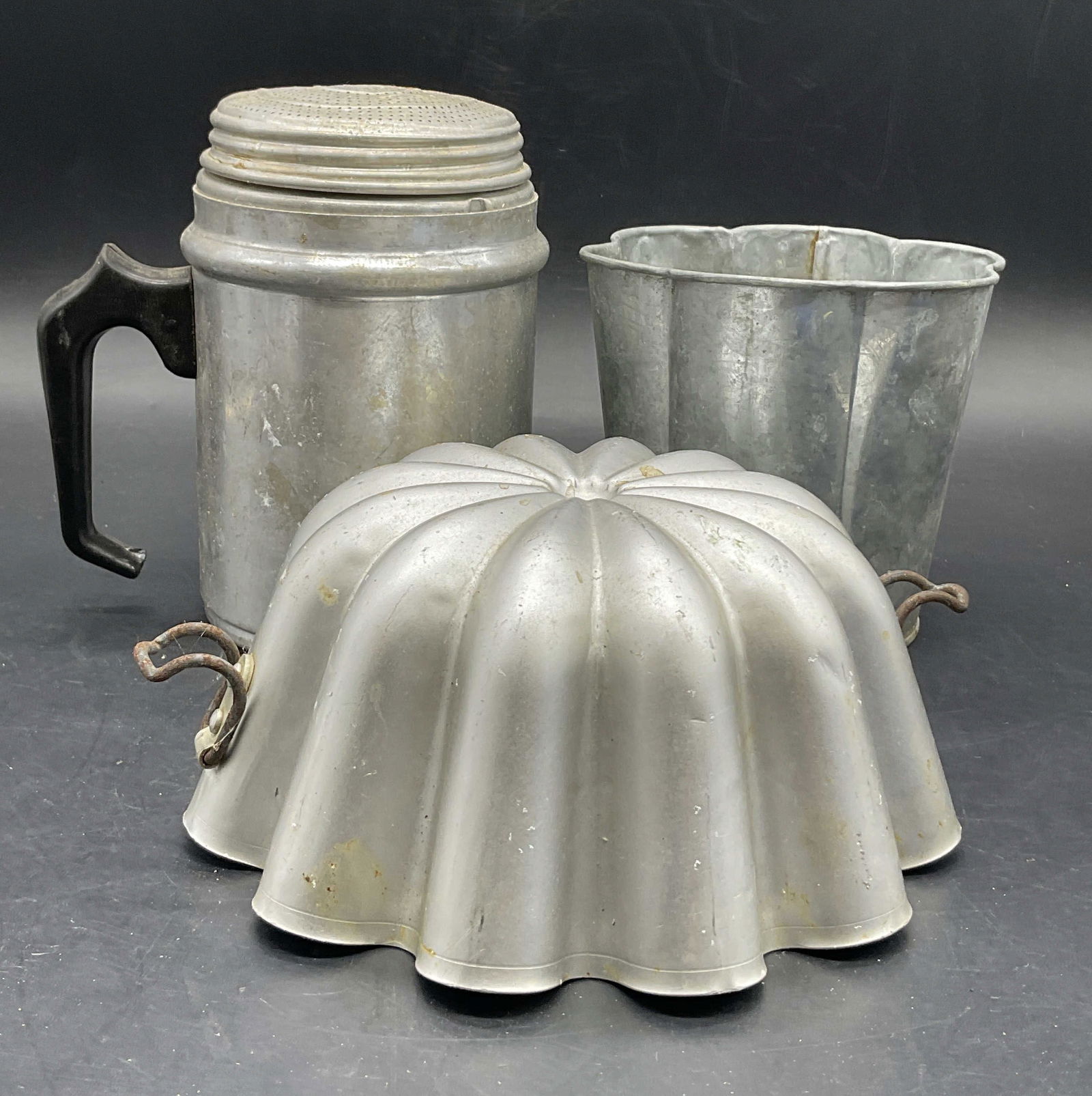 Lot3 Vintage Silver Tn Metal Kitchenware Tableware: Three pieces of Vintage Silver Toned Metal Kitchenware / Tableware. One seasoning dispenser, one mold, and one scallop rim vessel. Seasoning dispenser measures approx. 6H x 5W in. Denting, residue, di