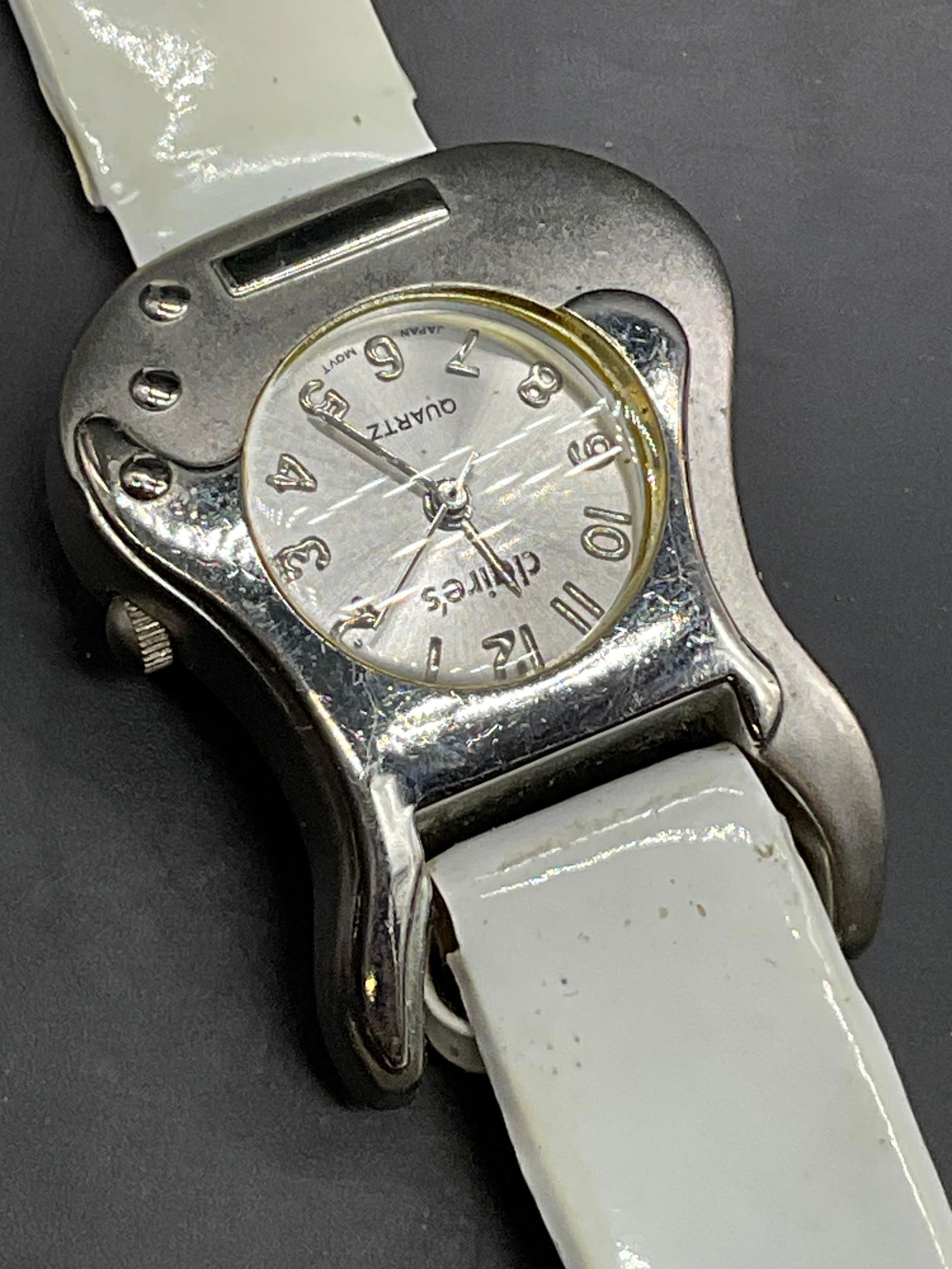 CLAIRES Quartz Guitar Motif Wristwatch: CLAIRES Guitar Motif Wristwatch. Silver tone metal guitar motif watch face with a white faux patent leather band. Length measured end to end approx. 8L in. Watch face reads CLAIRES Quartz. Not tested