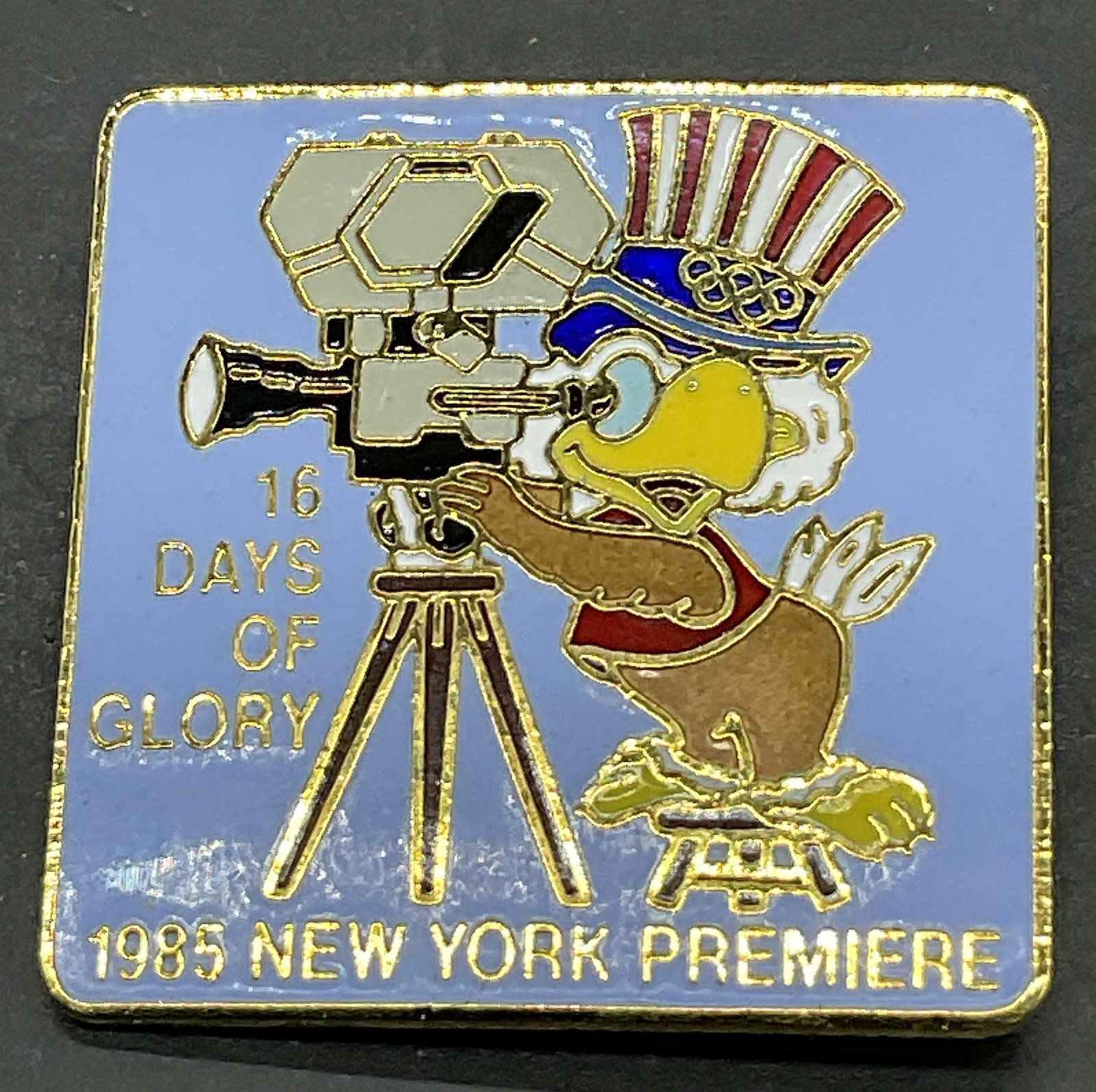 1980 LA OLY 16 Days of Glory 1985 NY Premier Pin: 1980 LA OLY .COM 16 Days of Glory 1985 NY Premier Enamel Metal Pin. Decorated with a patriotic bird motif. Obverse reads 16 Days of Glory 1985 New York Premier. Reverse reads 1980 LA OLY .COM. Measure