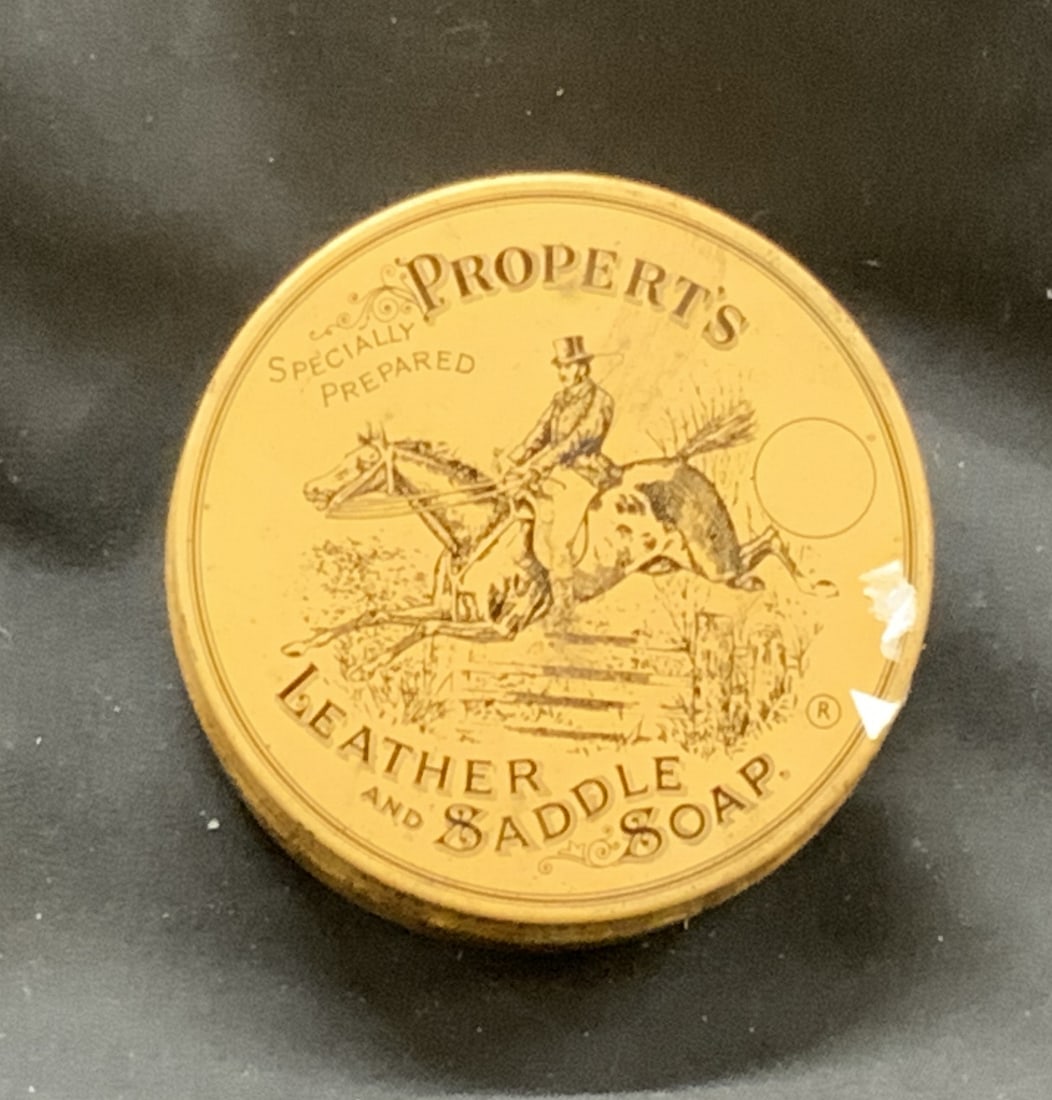 Vintage Properts Leather & Saddle Soap England: Vintage Properts Leather & Saddle Soap Round Sealed Container of leather cleanser and softener. Has wear and tear on container, rust throughout. Lid appears stuck. Made in England. Measurements: Width