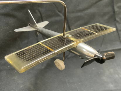 Solar Revolving Metal Airplane Toy: Airplane toy is silver toned and metal. Solar revolving airplane toy with circular form base. Plane figure has front propeller and wheels. Piece measures approximately 15.5 inches long 7.5 inches tall