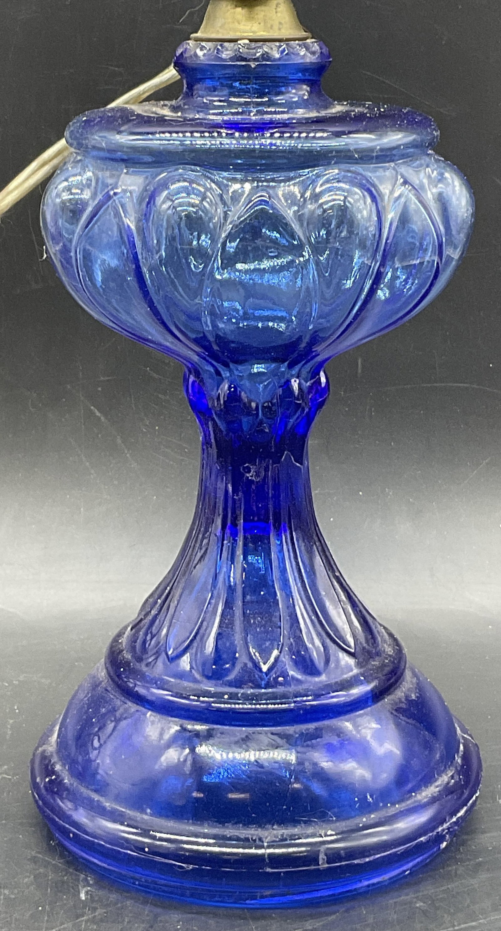 Vintage Cobalt Blue Glass Table Lamp: Vintage Cobalt Blue Glass Table Lamp. Corded. Metal hardware to the piece. Measures approx. 19H x 4W in. Height includes harp. Seam present. Cracking to glass. Losses to metal and surface wear present