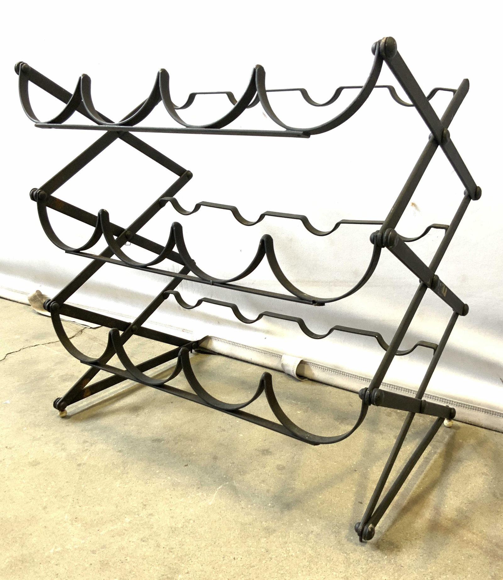 Folding Vintage Metal Wine Bottle Rack: Wine bottle rack is vintage. Piece is black toned And metal. Wine rack folds. Piece has space for 12 bottles. Rack measures approximately 18 inches wide and tall 11.5 inches deep. Wine rack, metal win