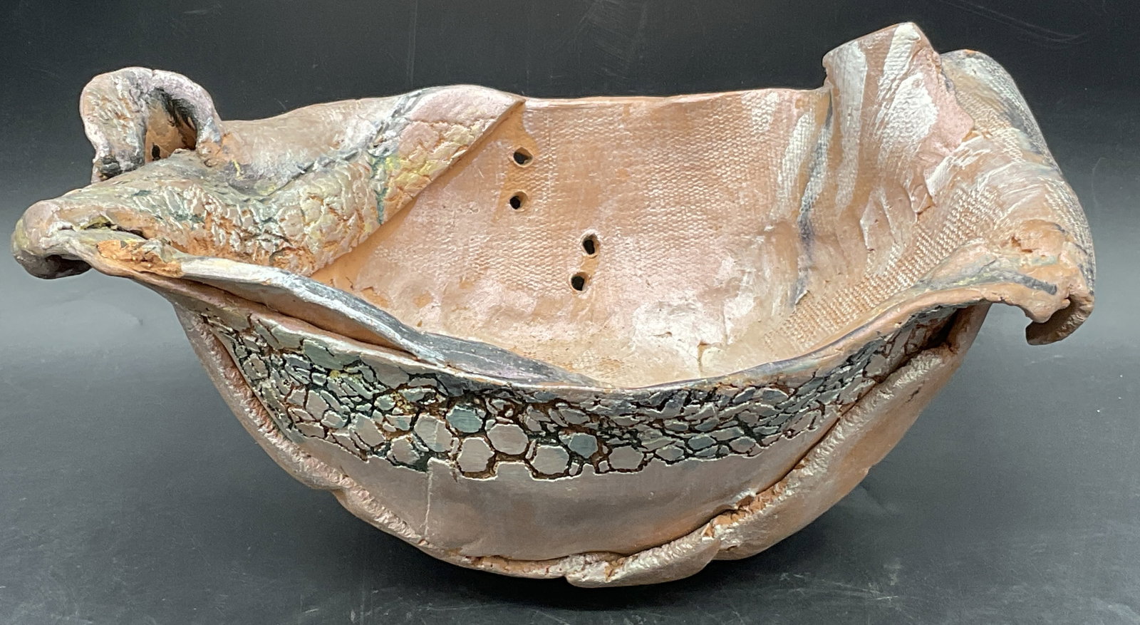 Vintage Handmade Pottery Bowl: Vintage Handmade Pottery Bowl. Rustic design features texture, drilled holes, folds, and multicolored hues. Underside marked 4B. Measures approx. 4.25H x 10W in. Felt to underside. Chipping, losses, a