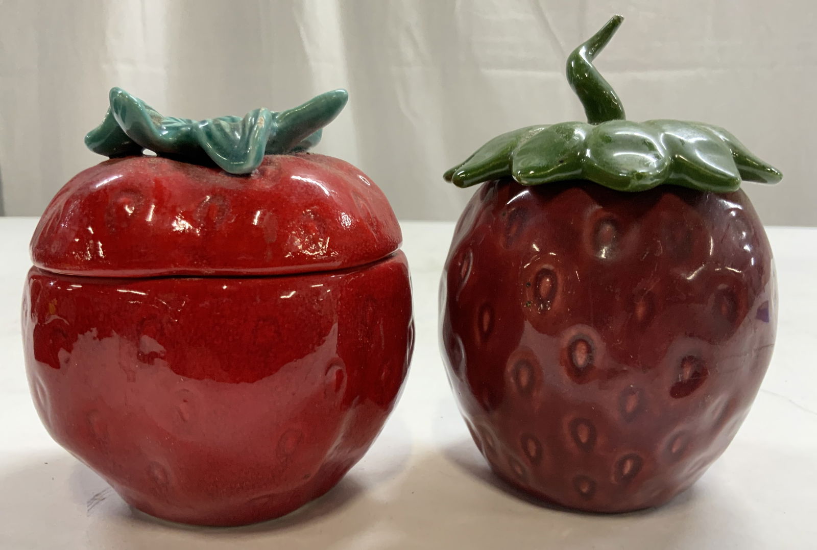 Lot 2 Porcelain Strawberry Jars W Lids: Lot includes 2 strawberry form jars. Each appear to be porcelain possibly ceramic. Each piece includes lids. Jars each appear be hand painted. Slightly larger jar measures approximately 4.25 inches ta