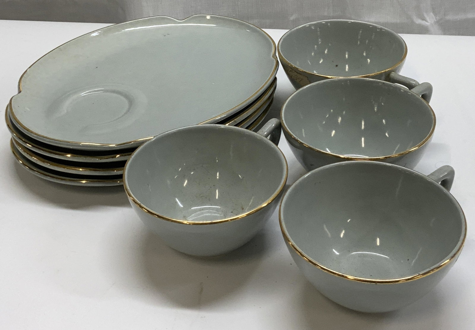 Group Lot 8 Ceramic Saucers & Cups.: Group Lot 8 Ceramic Saucers & Cups. 4 ceramic cups, and 4 ceramic saucers/desert plates. They all have a light blue/greyish color with a gold rim. Visible residue on plates & cups. Including some disc