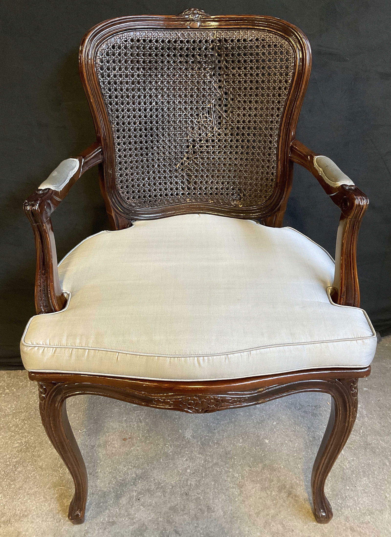Vintage French Style Caned Upholstered Armchair: Vintage French Style Caned Upholstered Armchair. Carved floral details to the wood frame. Caning to the back and seat. Soft hand light gray upholstery to the arms and to the removable cushion. Chair m