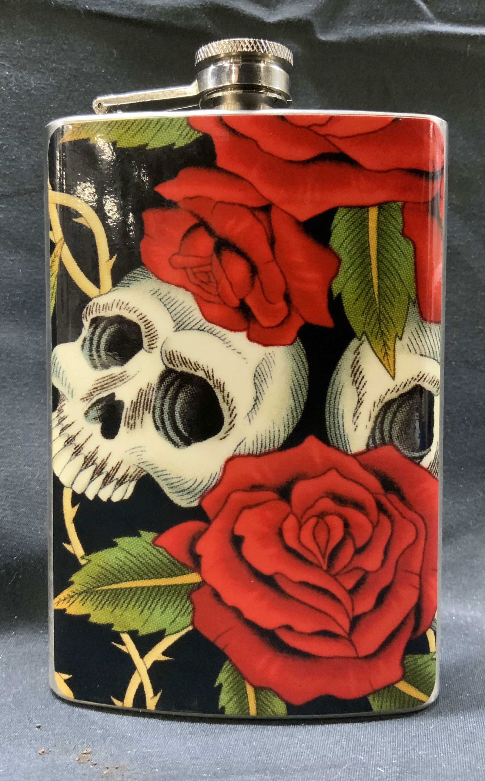 TOPSHELF FLASKS Stainless Steel Skull Floral Flask: TOPSHELF FLASKS Stainless Steel Skull Floral Flask Stainless steel flask, has an image of skulls with red flowers and thorns. Underside of flask reads, TOPSHELF FLASKS, Stainless Steel 8oz. Measuremen