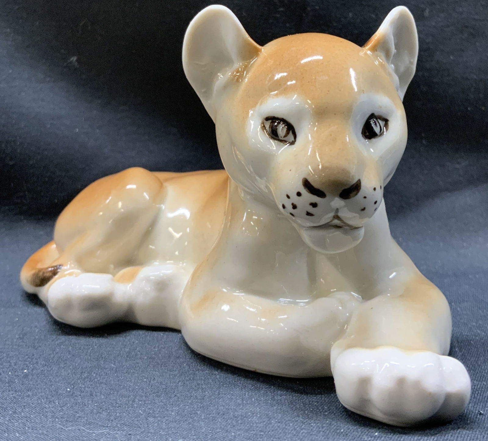 Vintage Porcelain Lion Cub Figurine: Vintage Porcelain Lion Cub Figurine Lion club figurine that is laying down and has its head up. Has a golden brown and beige shiny color. Measurements: length 5.2in x width 2in x height 3in Porcelain