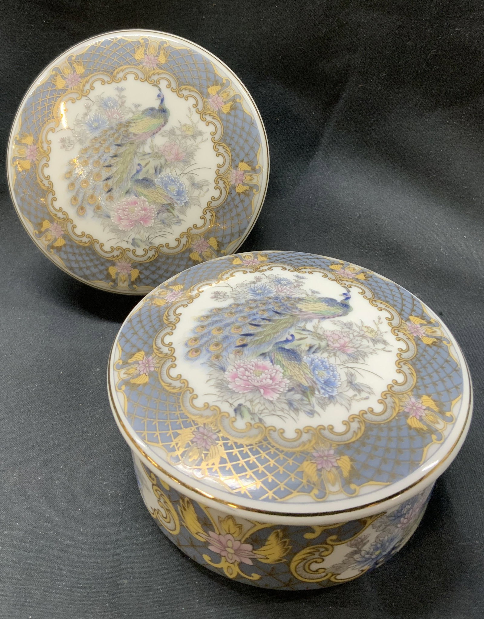 Lot 2 Porcelain Peacock Trinket Box: Lot 2 Porcelain Peacock Trinket Box. 2 trinket boxes with images of peacocks on the lid and base. Including a floral & gold pattern. Lid has a gold trim. No visible signature. Surface wear consistent 