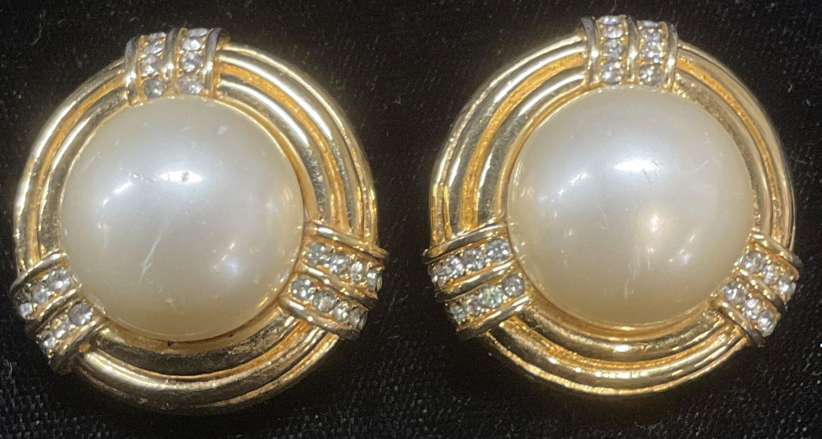 Vtg CINER Gold Tn Faux Pearl Earrings: Vintage Ciner gold tone round clip on stud earrings with faux pearl cabochon and colorless crystal. Signed on underside. Measure approx 1.25 inches wide. Some wear including scratching observed. Jewel