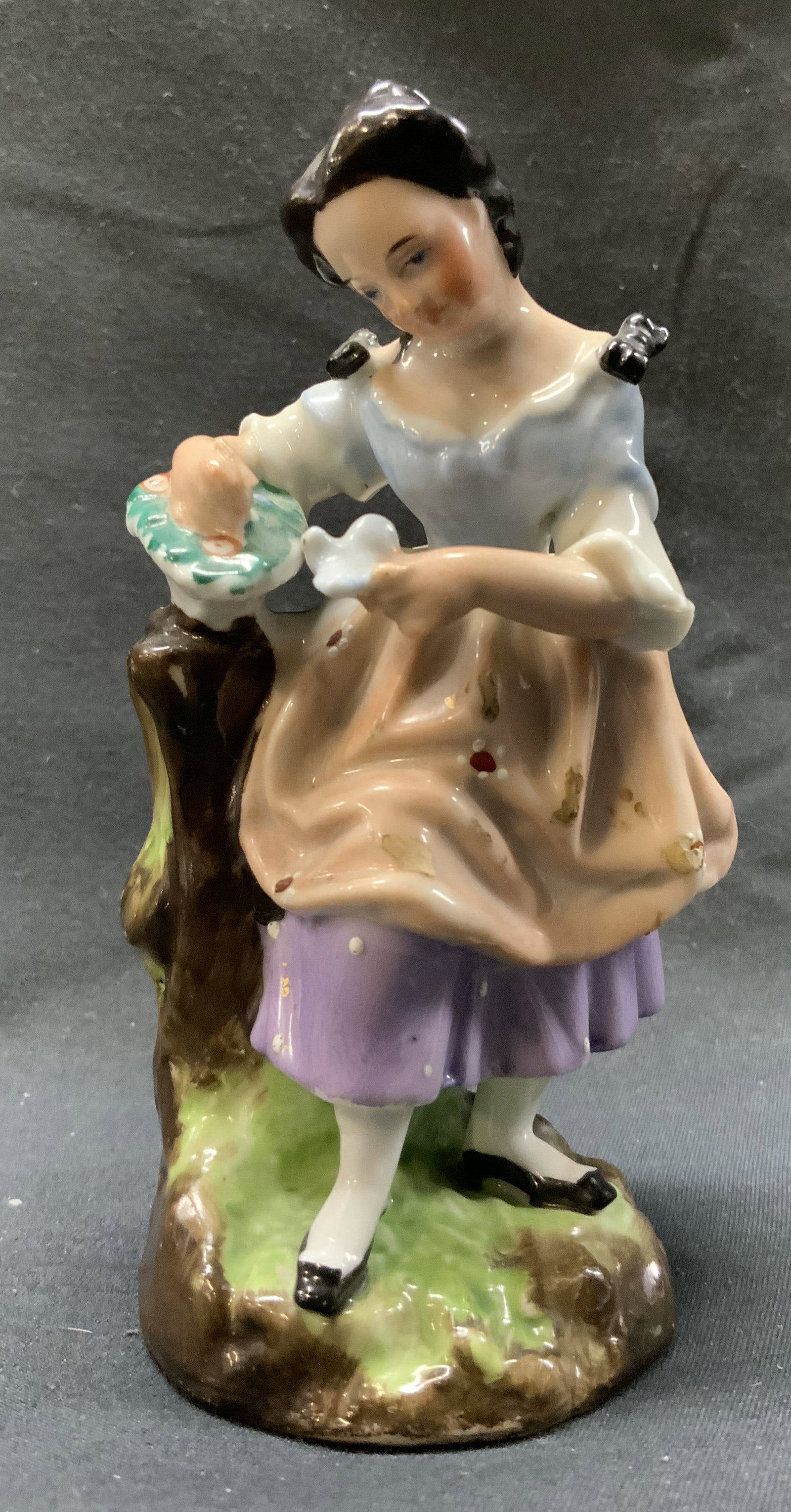 Signed Vintage Porcelain Women Figurine: Vintage Porcelain Women Figurine.Porcelain women figurine. Women is standing on a green and brown base, appears to be a rock. She’s wearing a blue top & pink skirt, while holding a white bird. Figur
