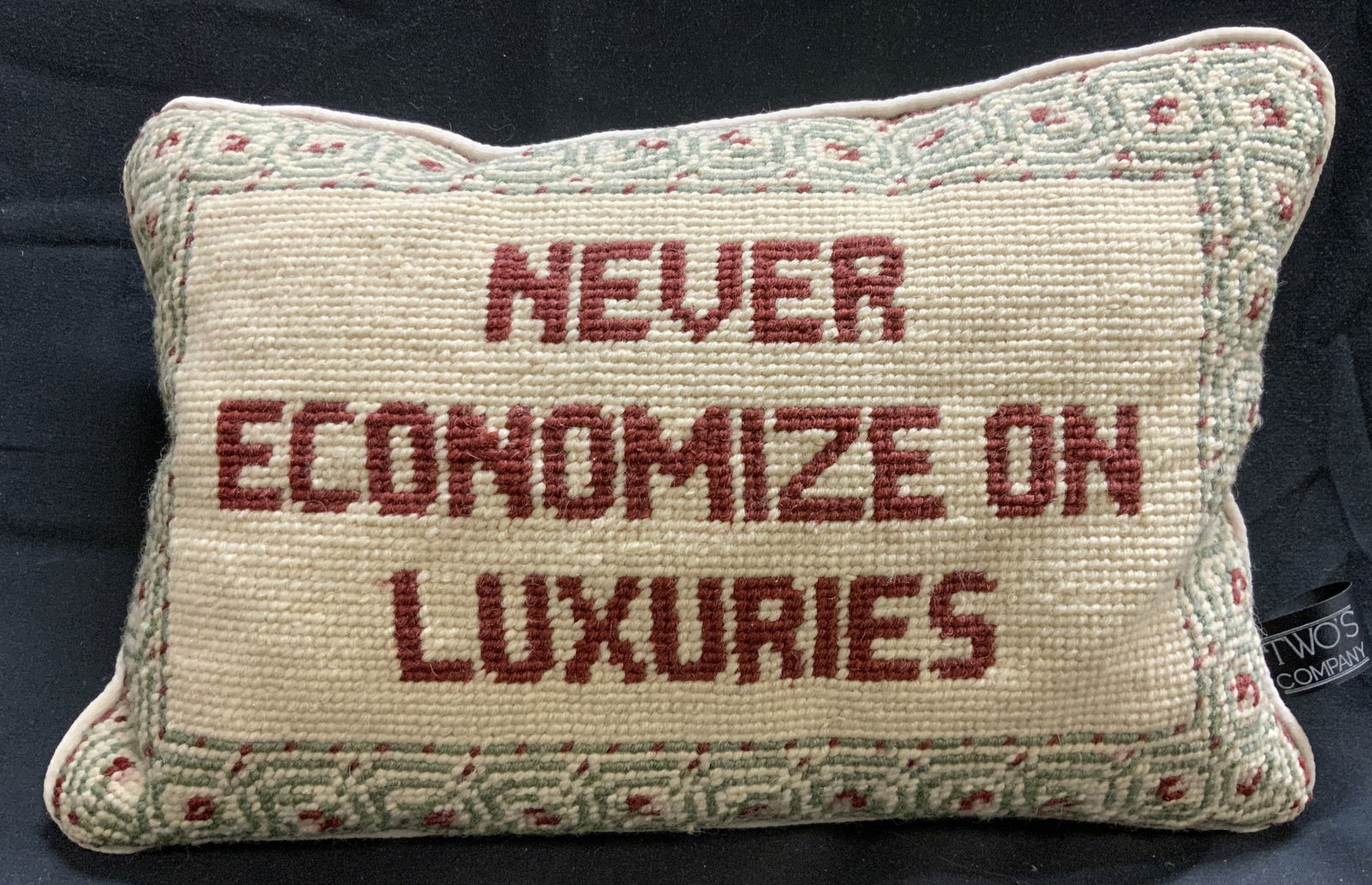 TWOS COMPANY Never Economize On Luxuries Pillow: Tag reads TWOS COMPANY. Pillow has needlepoint side. Edges of pillow has welting. Pillow reads NEVER ECONOMIZE ON LUXURIES. Edges have red and green patterned detail. Pillow measures approximately 12