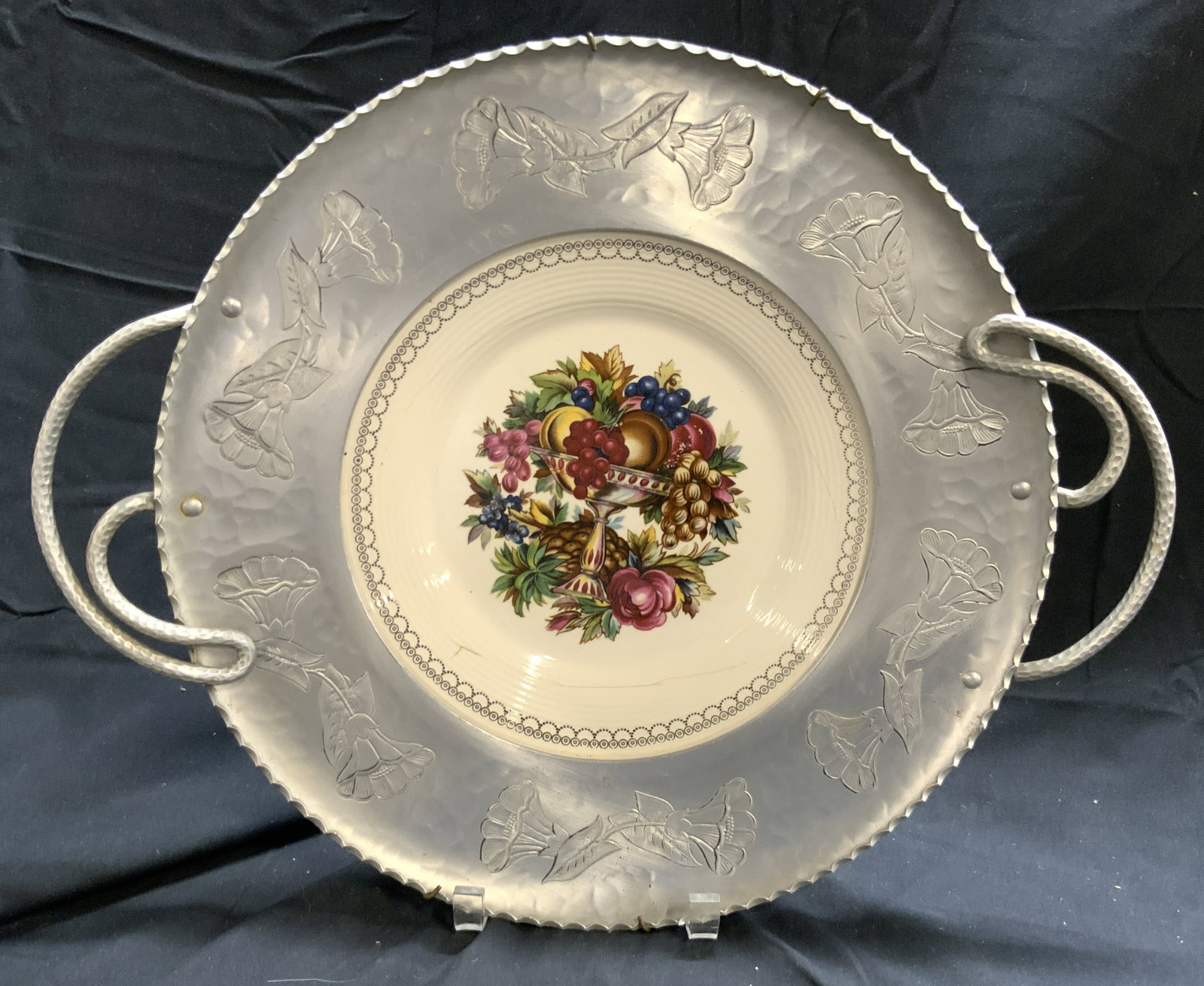 TRIUMPH LIMOGES Porc Plate W Metal Rim USA: Underside is marked TRIUMPH LIMOGES MADE IN USA. Plate is vintage and porcelain. Piece has attached silver toned metal rim with floral relief detail and handles. Plate has fruit arrangement detail. Pi