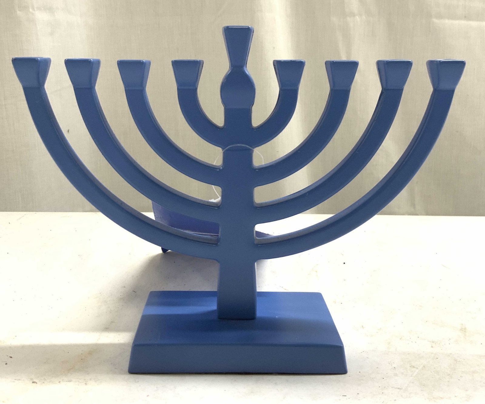SPRITZ Blue Composite Judaica Menorah Org Tag: Tag reads SPRITZ MENORAH. Menorah is blue toned and appears to be composite. Underside has black toned felt lining. Base has rectangular form. Menorah measures approximately 7.5 inches wide, 5.75 inch