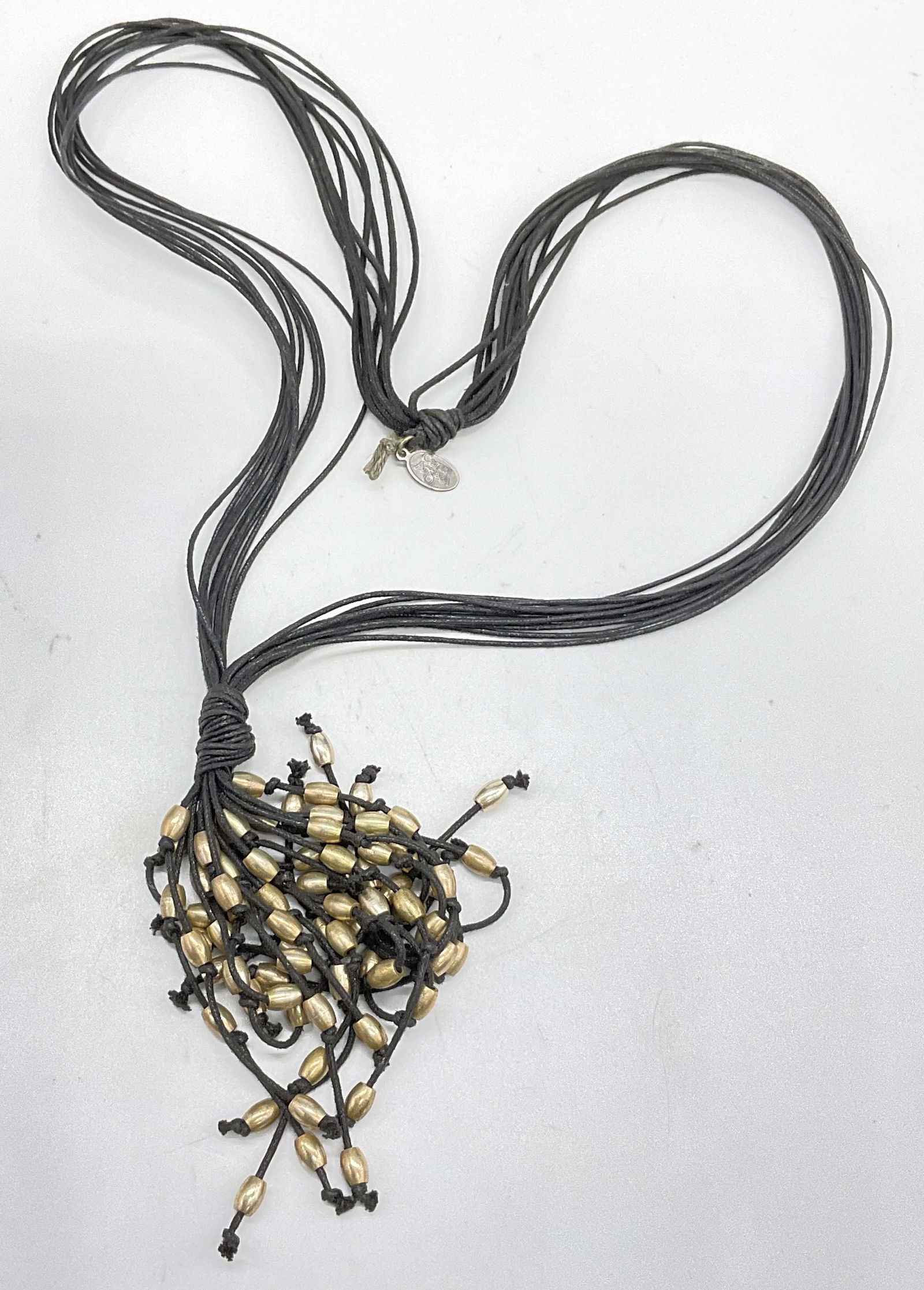 CARME ANGLADA Beaded Black Cord Necklace: CARME ANGLADA Beaded Black Cord Necklace. Gold tone metal beads are interspersed throughout the end of the necklace. Knot accents to the piece. Silver tone metal charm reads CARME ANGLADA. Drop length