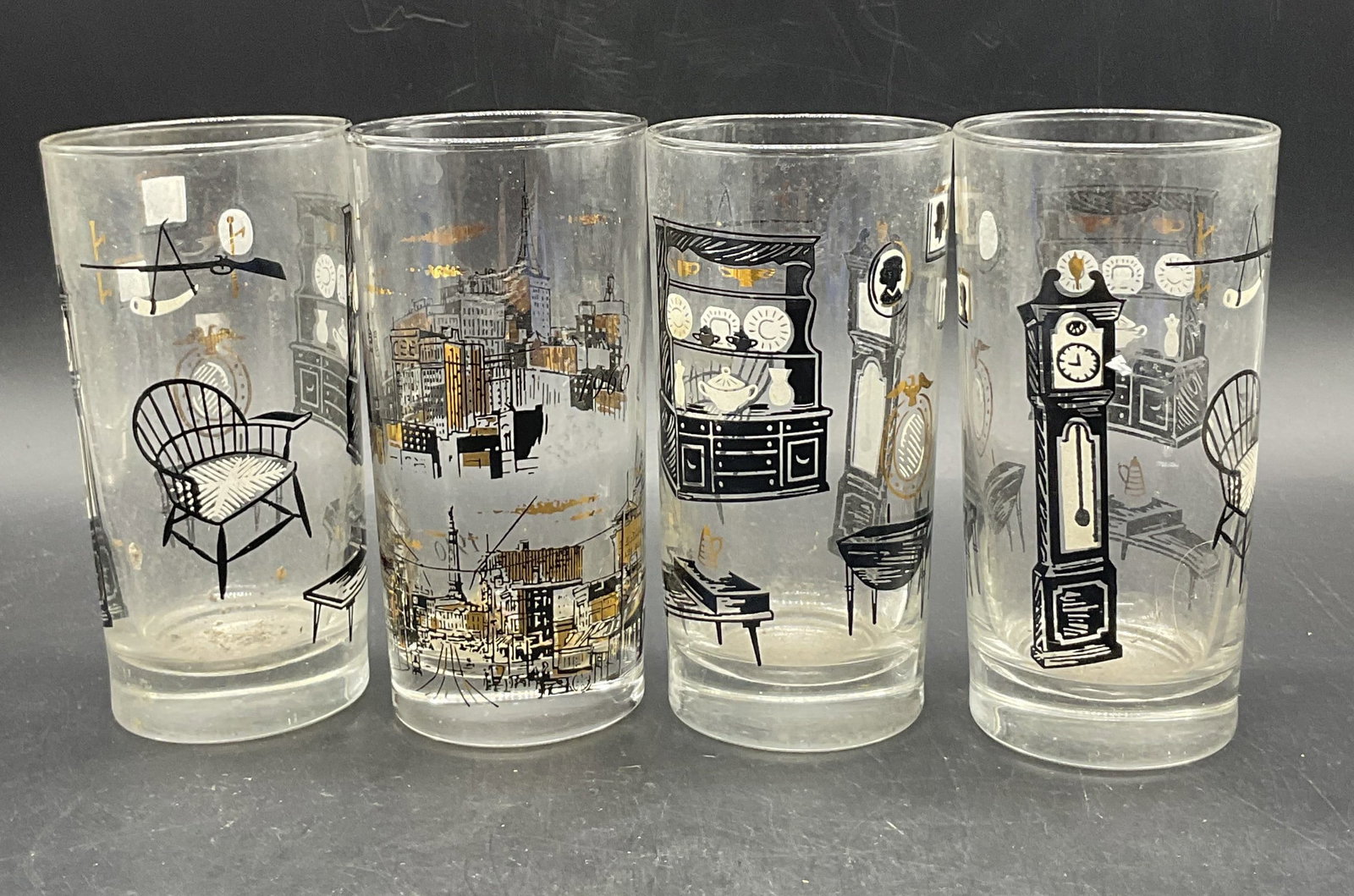 Lot 4 Vintage Americana Highball Glasses, Barware: Four Vintage Americana Highball Glasses. Americana theme to the glasses. Includes a glass with a city scene and glasses with a living room scene. Crafted from glass. Features black, white, and gilt de