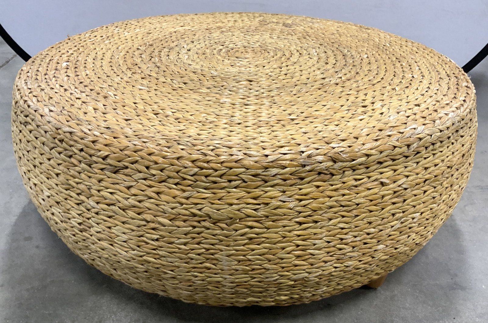 LEVENGER Circular Woven Rattan Ottoman 38in D: Underside is marked LEVENGER. Ottoman is tan toned crafted with woven rattan. Piece has circular form. Ottoman has 4 tan toned wooden feet. Piece measures approximately 38 inches diameter 15 inches ta