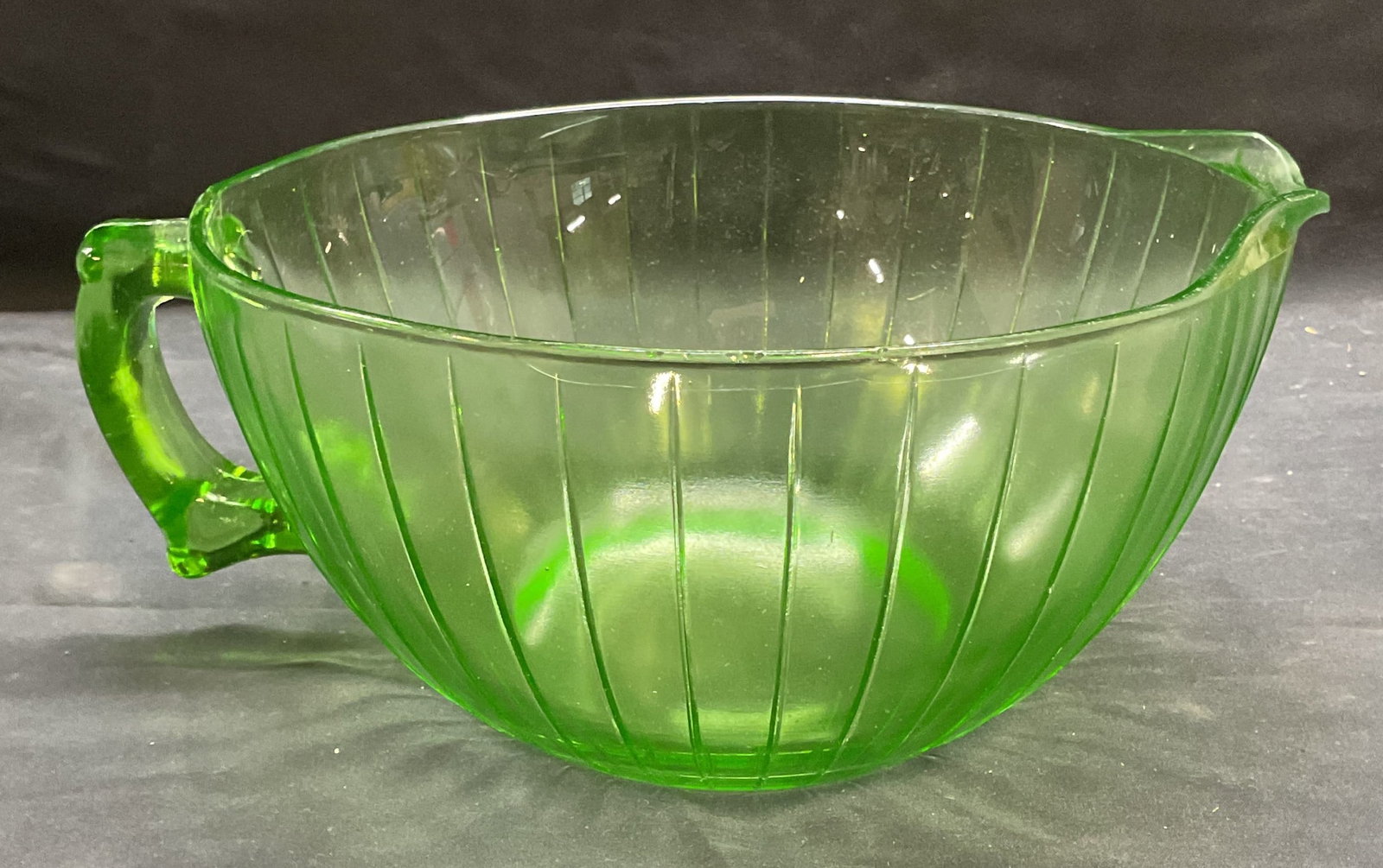 Vintage Uranium Depression Glass Mixing Bowl: Vintage green uranium depression glass mixing bowl with handle. Ribbed pattern. Measures approx 8.5 x 4.5 inches. Some scratching observed. Chipped on rim. Uranium glass, uranium glass mixing bowl, mi