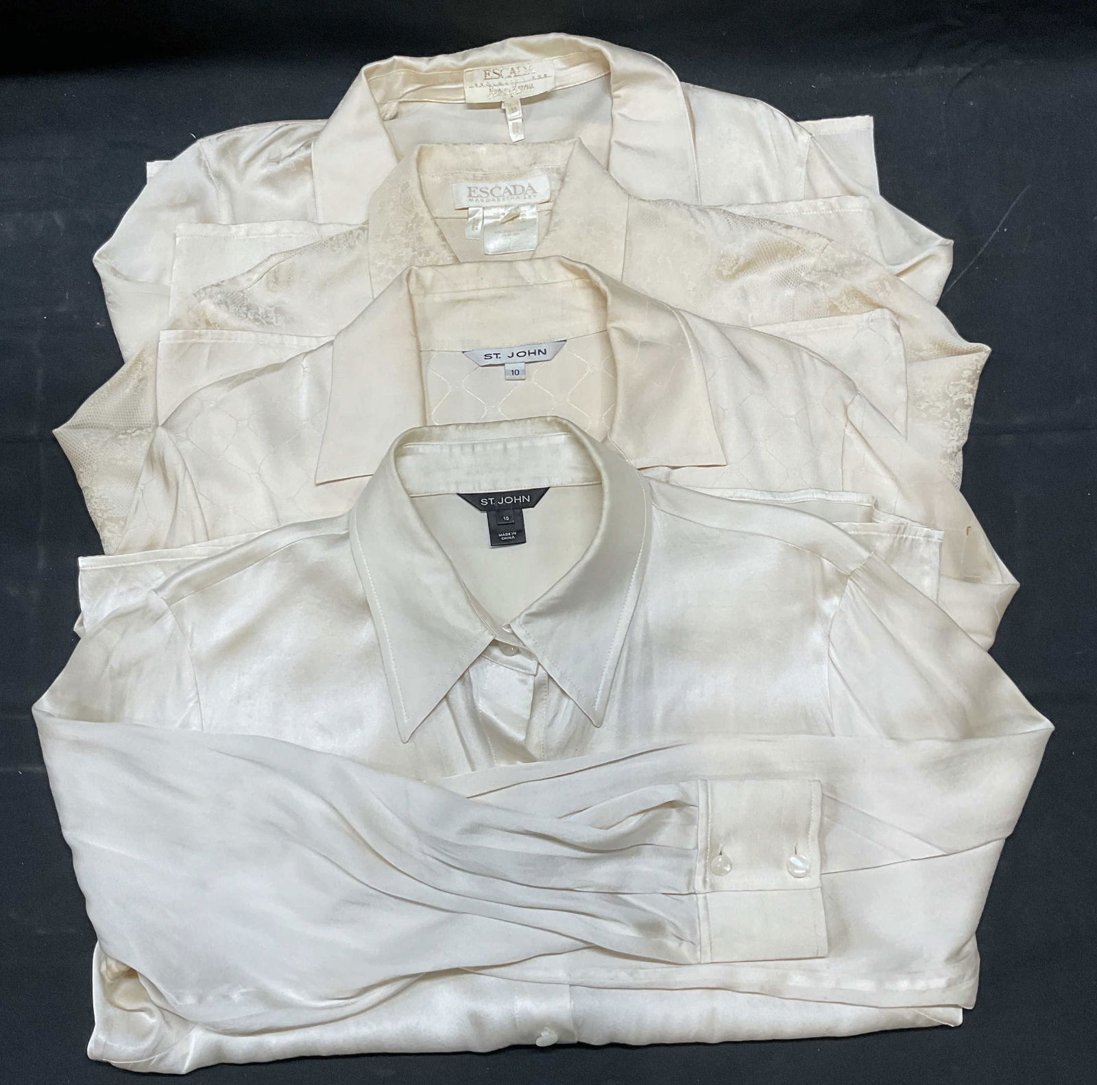 4 St John, Escada White Silk Button Up Tops: Lot of 4 white silk long sleeve button up tops. Labels includes St John and Escada. Sizes marked 36, 38, and 10. All tops have wear including, pulls, blemishes, and discoloration. One top has replacem