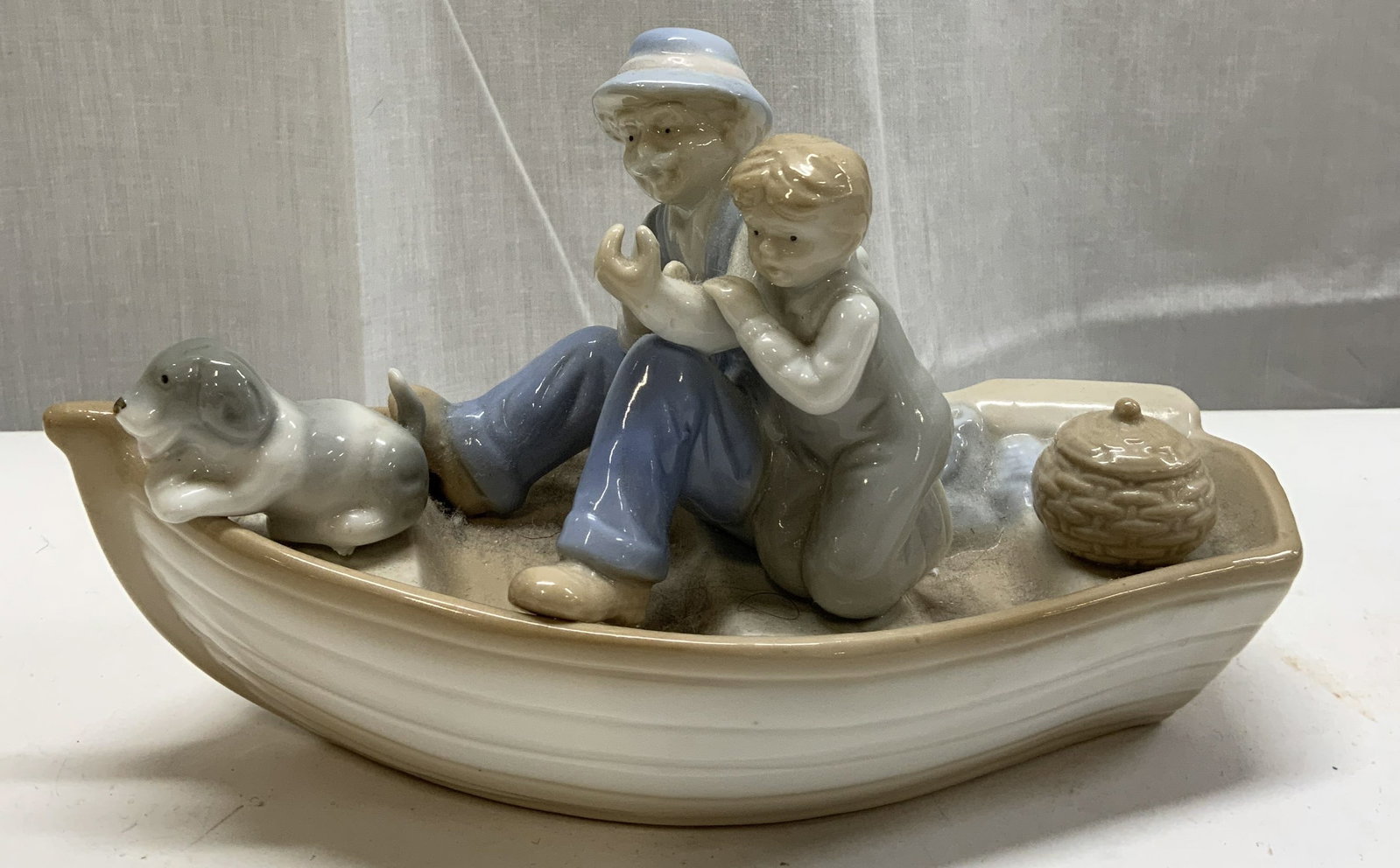 Meico Old Man & Boy Fishing Boat Porcelain Figural: Meico Old Man & Boy Fishing Boat Porcelain Figural Porcelain figural depicting an old man wearing a blue & white suit, a boy wearing grey overalls sitting in a boat. Including a dog & basket. Undersid
