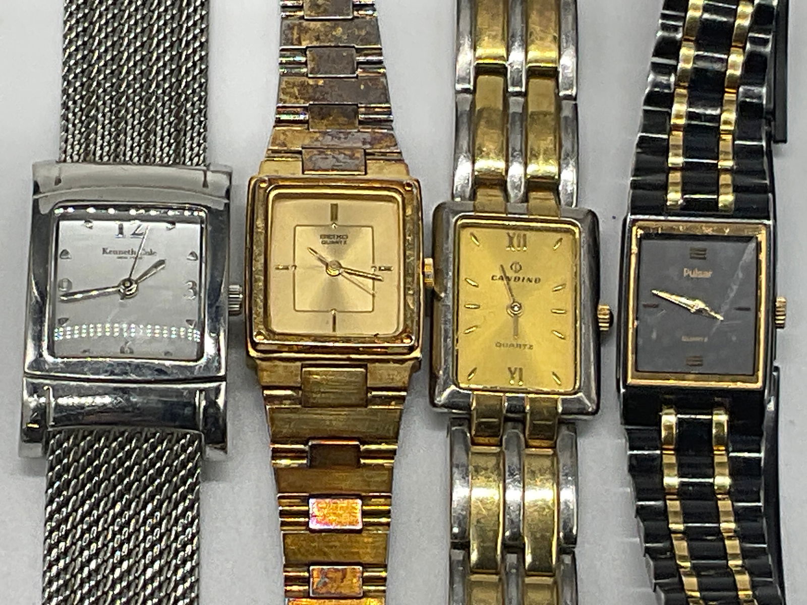 Lot 4 PULSAR, SEIKO, CANDINO, K. COLE Wristwatches: Four rectangular faced metal wristwatches. Brands include KENNETH COLE, PULSAR, SEIKO and CANDINO. Black, gold, and silver tone metal hues to the pieces. The watches have stainless steel backings. Lon