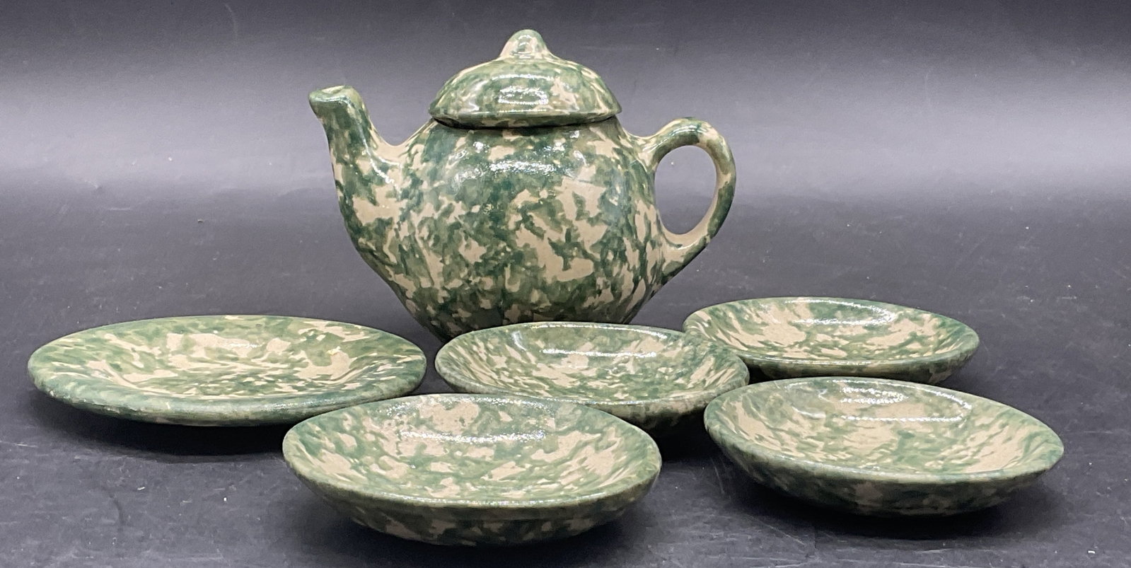 6 Vintage Signed Spongeware Pottery Tea Set: A six piece spongeware demitasse tea set. Includes a lidded teapot and plates. Primarily green and cream hues. Largest plate measures approx. 3.5L x 3.5W in. The underside of the teapot is signed, ill