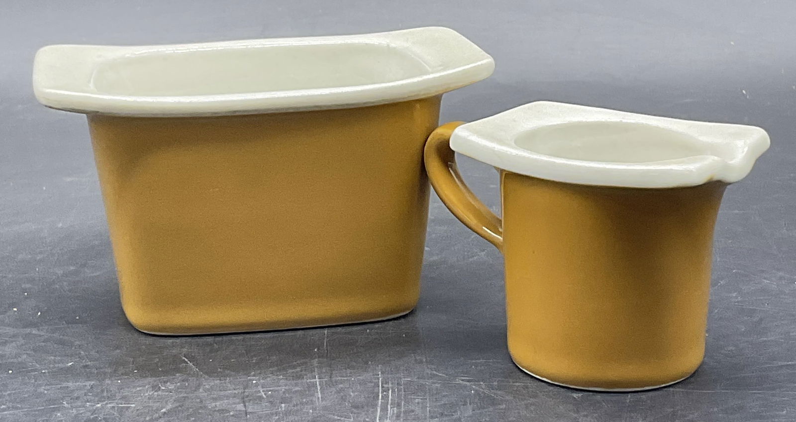 HALL USA Vintage Ceramic Sugar Bowl & Creamer: HALL USA Vintage Ceramic Sugar Bowl & Creamer. White hued interior and light brown hued exteriors. Sugar bowl measures approx. 2.5H x 4.25W in. Undersides are marked HALL, MADE INUSA. Surface wear con