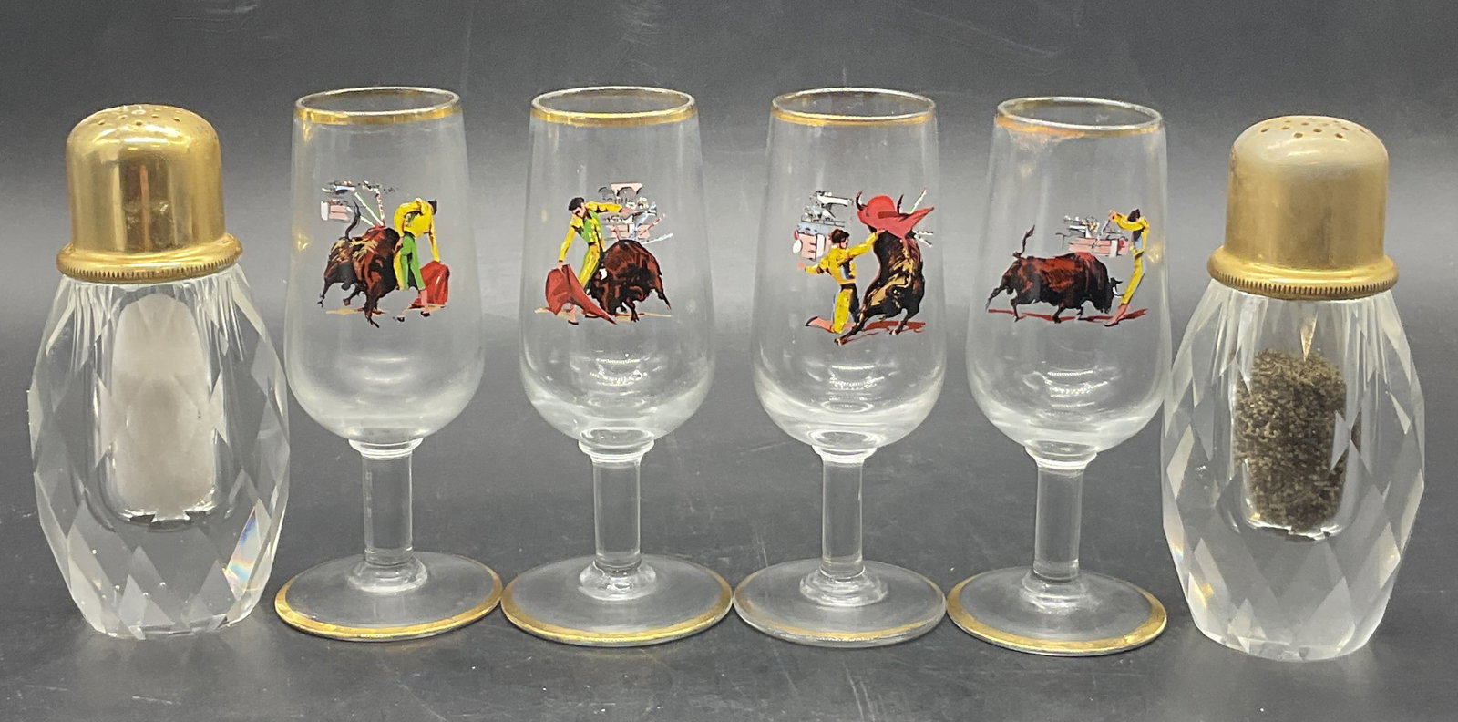 Lot 6 Glass Tableware, Stemware & Shakers: Four pieces of glass stemware with matador motifs and a pair of salt & pepper shakers with gold tone metal caps. The stemware measures approx. 4.75H x 2W in. Losses to paint, surface wear, and bubbles