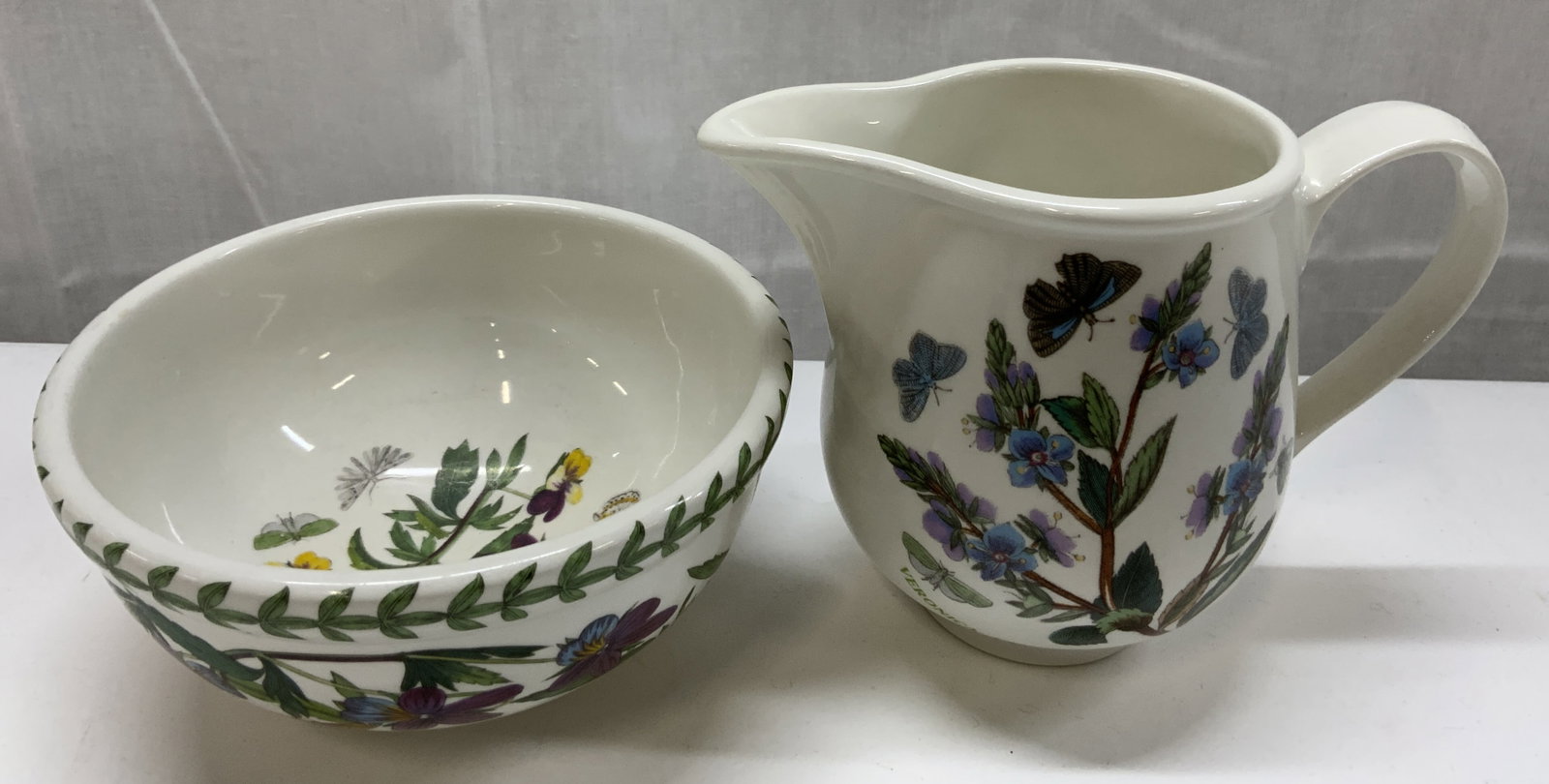 2 Portmeirion Botanic Garden Britain Creamer&Sugar: Portmeirion Botanic Garden Britain Creamer & Sugar Bowl. Sugar bowl with a green leaf border on the top rim. The interior of the bowl has purple & yellow flowers with butterflies. Creamer has blue flo