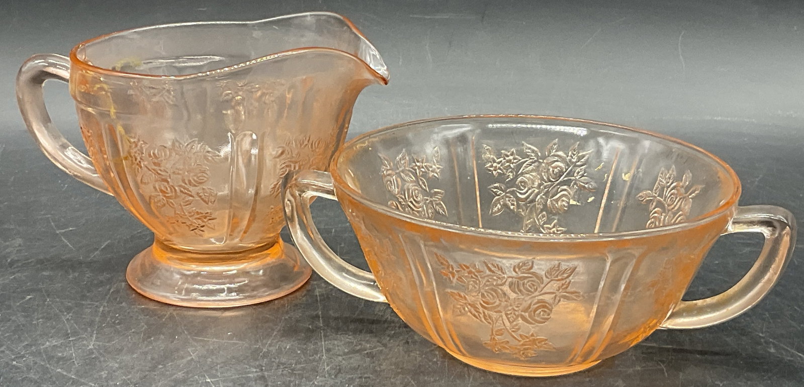 Vintage Pink Depression Glass Sugar Bowl & Creamer: Vintage Pink Depression Glass Sugar Bowl & Creamer Set. Lidless sugar bowl with double handle. Single handled creamer with spout. Both pieces feature floral motifs to the glass. Sugar bowl measures ap