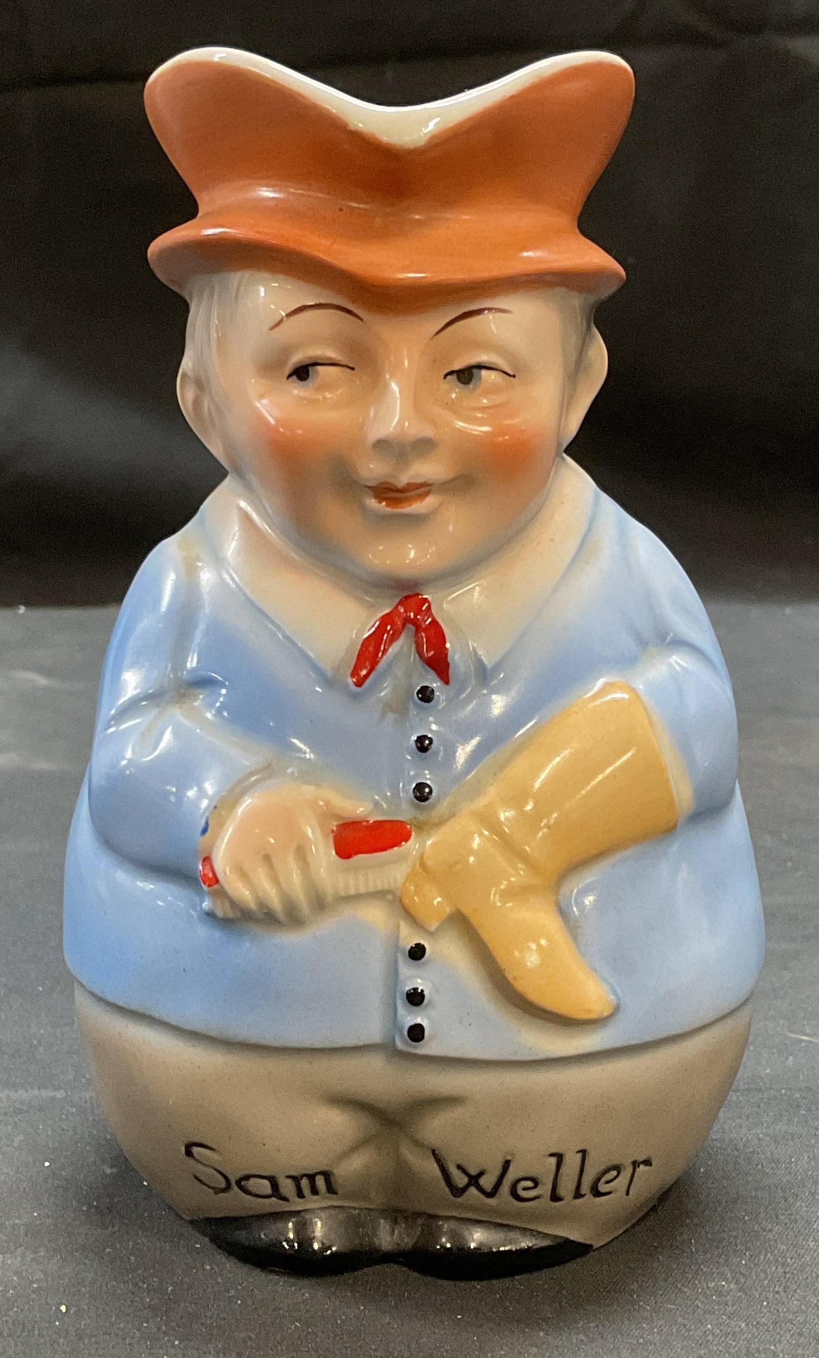 Vtg Porcelain Sam Weller Character Jug, Czech: Vintage porcelain Sam Weller character jug. Made in Czecho Slovakia. Hand painted in blue and orange. Figure of man cleaning boot. Measure approx 3.25 x 3 x 5.75 inches. Some wear including scratching