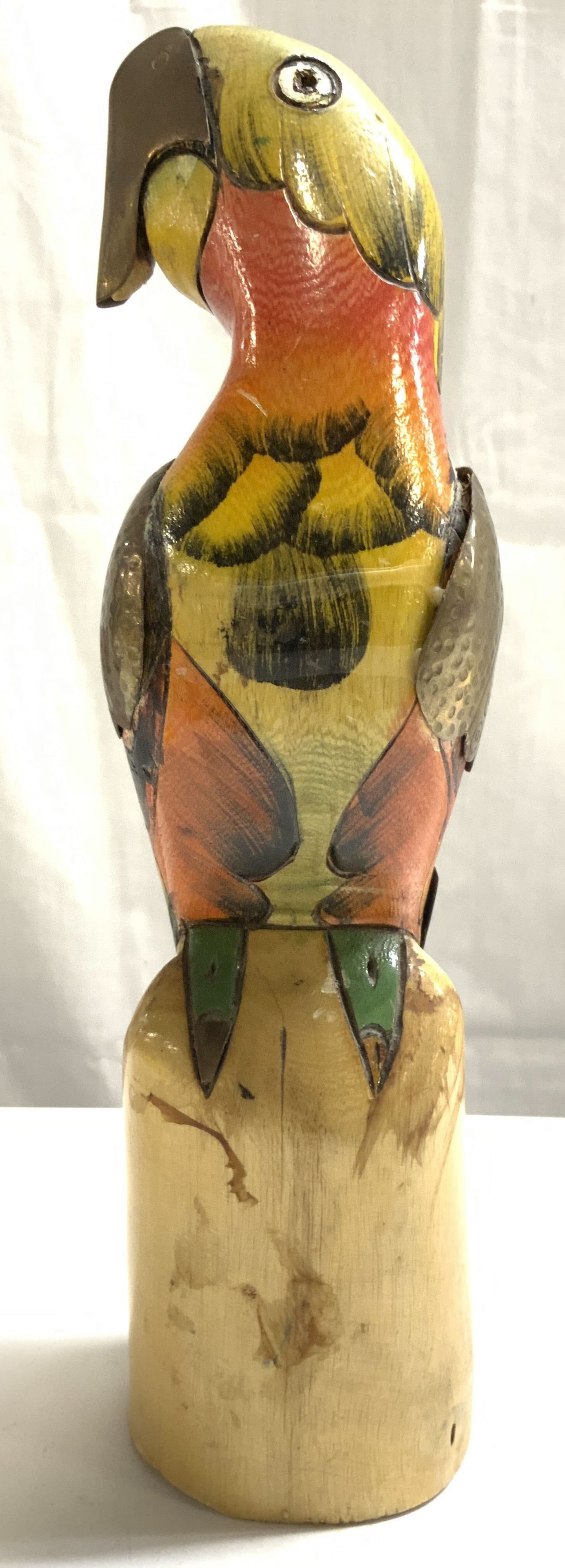 Vintage Carved Wooden Parrot Figure: Parrot figure is vintage. Piece is wooden. Parrot figure appears to possibly be hand painted. Depicts a parrot perched. Piece has gilt metal wings and tail feather. Piece measures approximately 11 inc