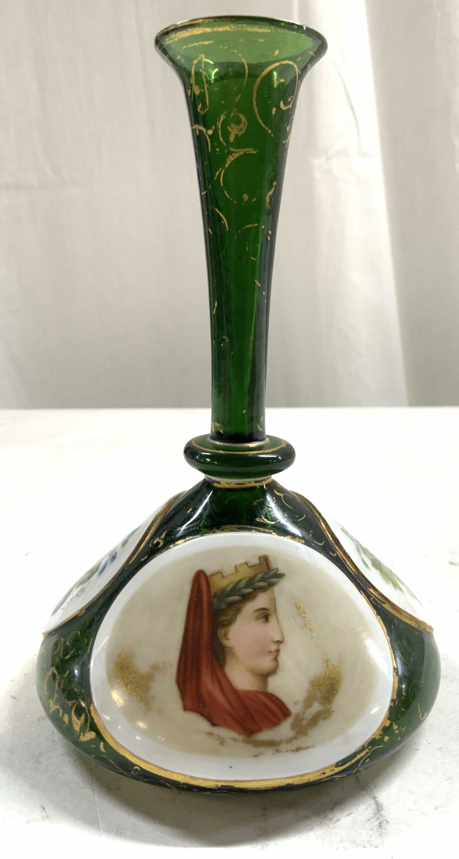 Bohemian Glass Emerald Art Glass Vase: Vase is emerald green toned & glass. Piece has 3 white toned areas with multi toned floral & leaf detail & 1 with profile image. Vessel has areas of gilt detailed. Piece appears to be vintage. Vase me