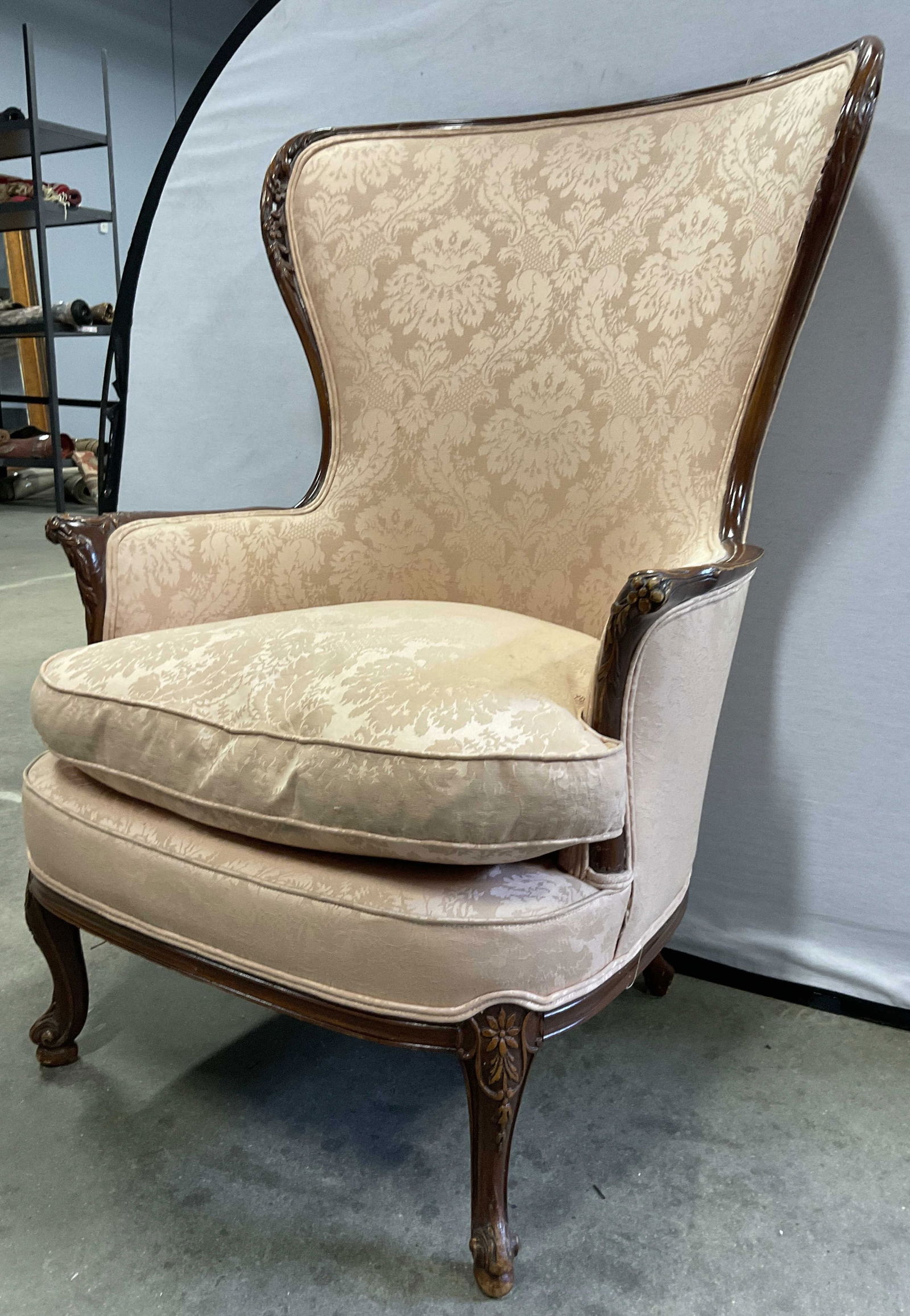 Vintage Upholstered Wooden Wingback Armchair: Vintage Upholstered Wooden Wingback Armchair. Light pink hued soft hand damask style upholstery to the piece. Removable cushion. Carved floral motif to the wooden frame. Discoloration, residue, surfac