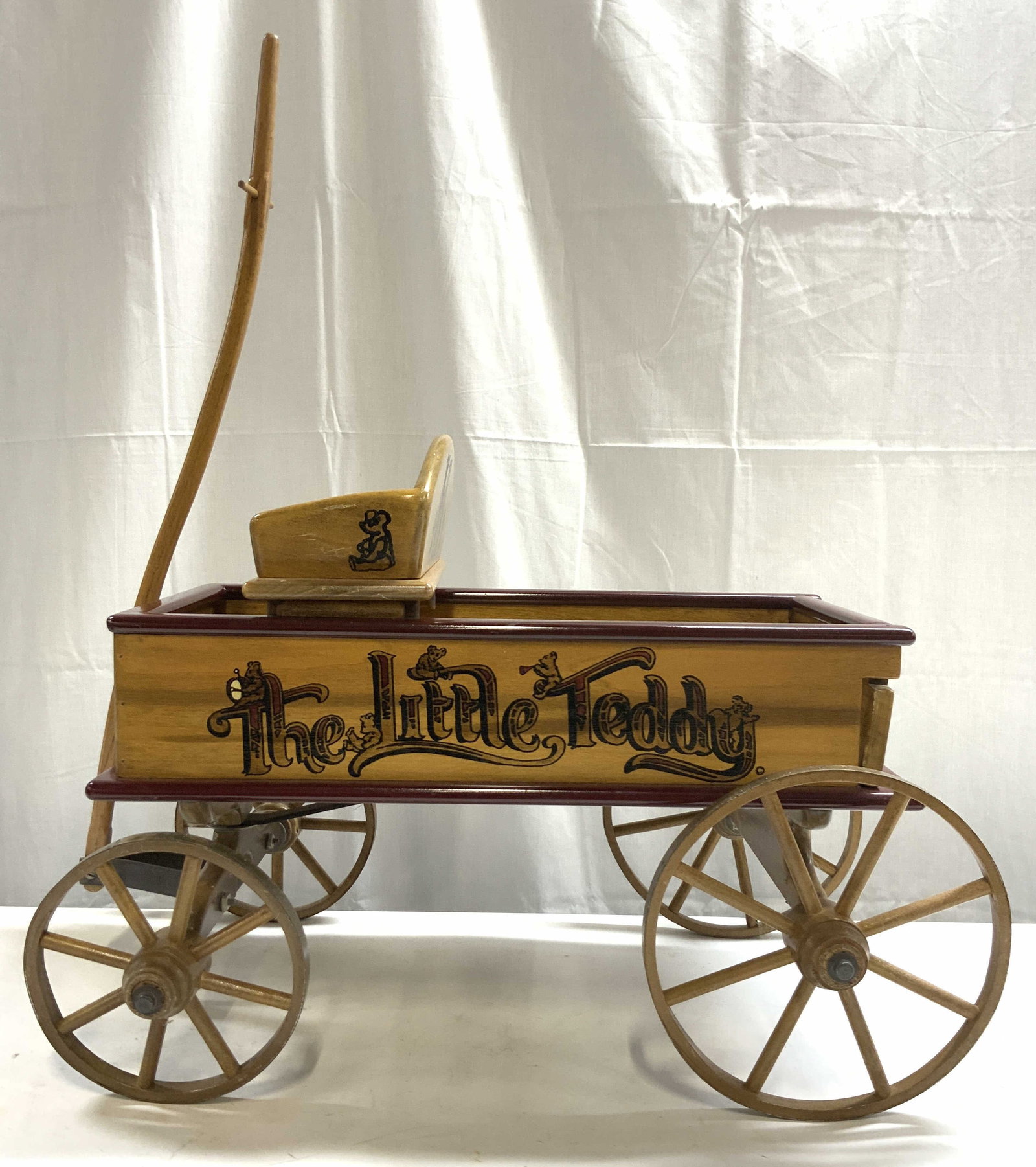 THE LITTLE TEDDY Vintage Wooden Wagon: Sides of piece read THE LITTLE TEDDY. Wagon is vintage and wooden. Wagon has seat. Piece has 4 spoked wheels. Backside is removable. Piece has wooden pull. Piece measures approximately 23 inches deep 