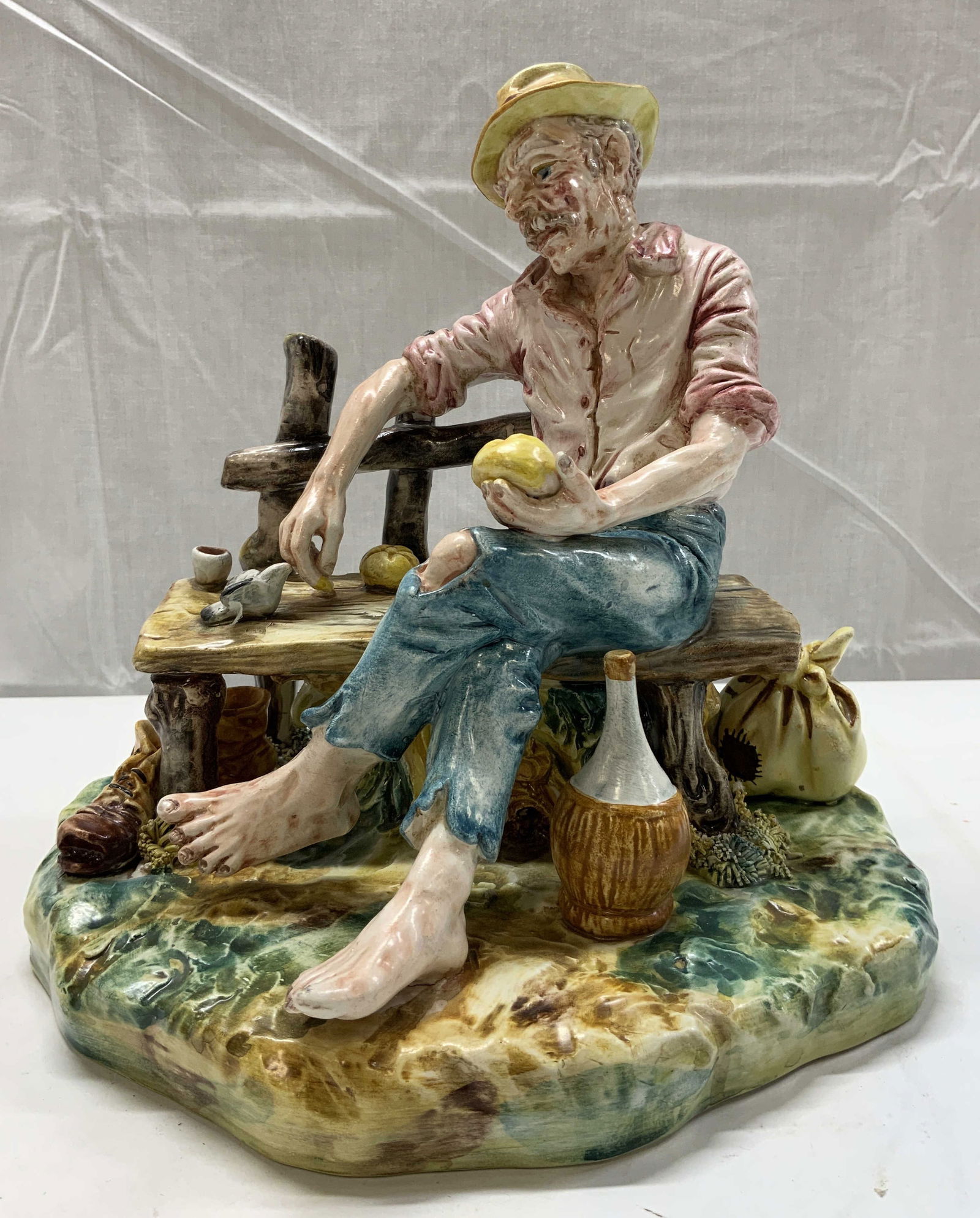 Capodimonte Porcelain Bench Figurine Man ITALY: Capodimonte Porcelain Bench Figurine Man ITALY Porcelain figurine depicting an old man sitting on a wooden bench. Man appears to be holding a loaf of bread in his hand. He is wearing a yellow hat, his