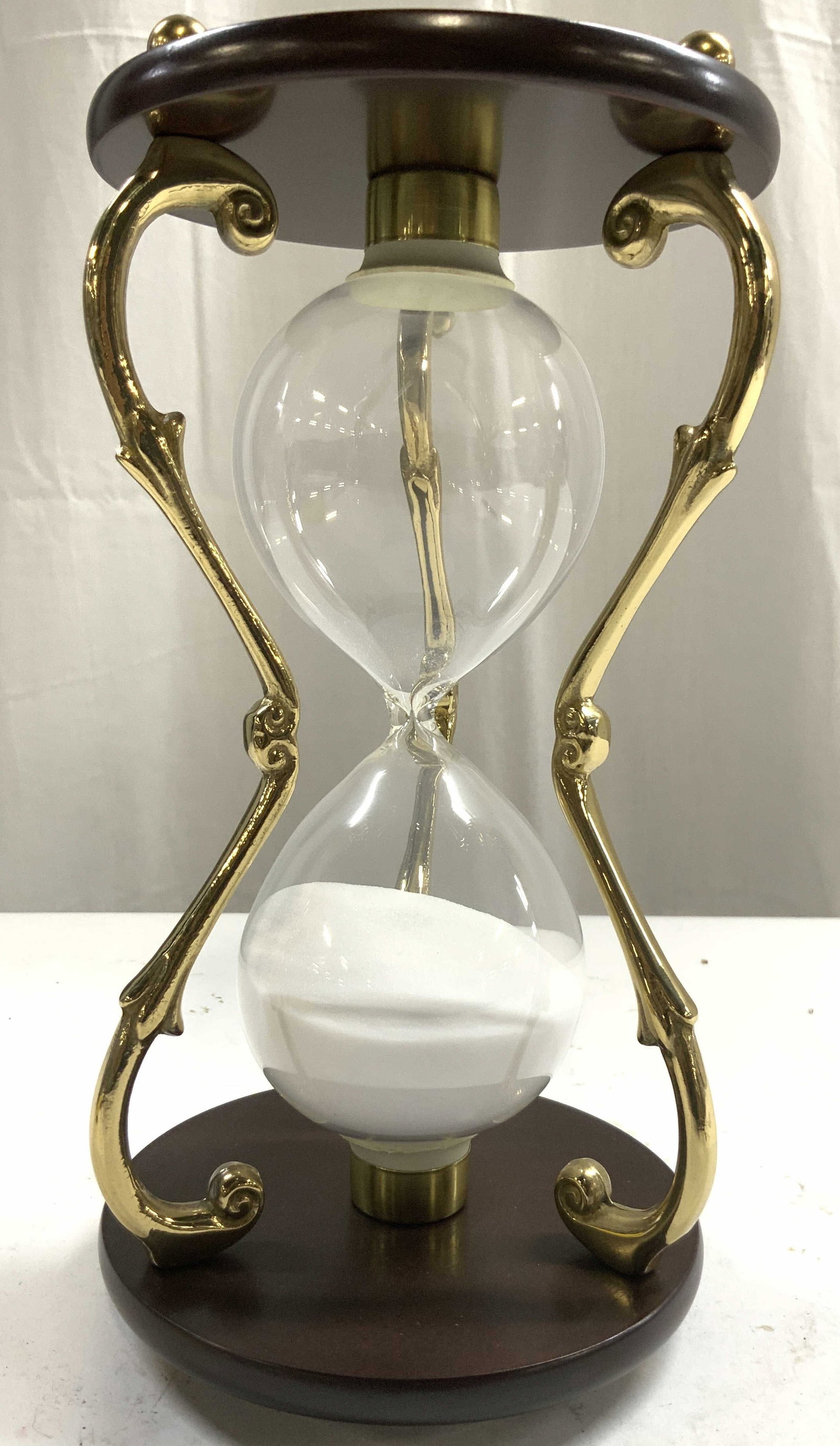 Wood Gilt Metal & Glass Hour Glass: Hour glass is crafted from brown toned wood with gilt metal supports and spherical form feet. With glass center. Sand on interior is white toned. Piece has 3 feet. Ends of gilt metal supports are scro