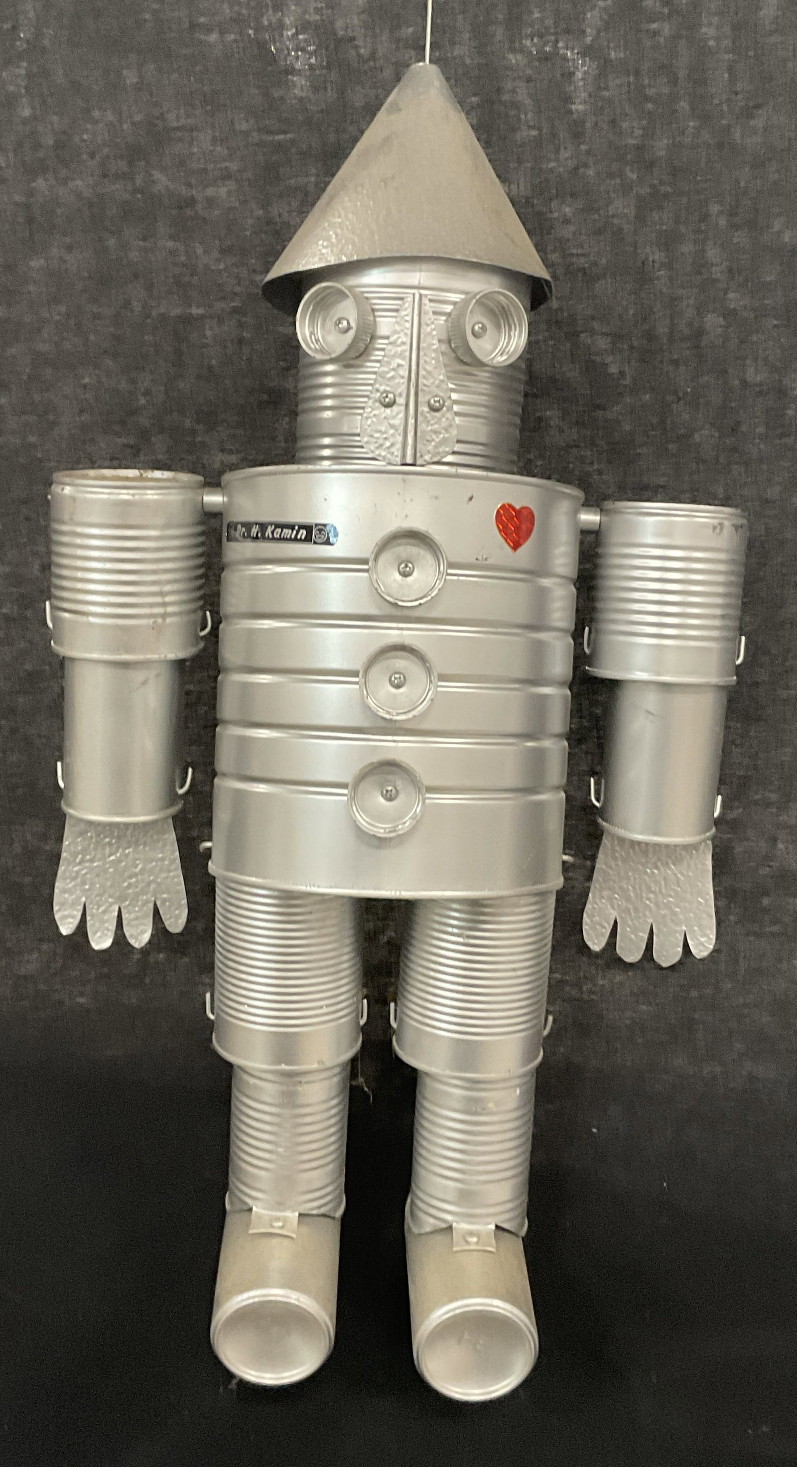 Handmade Articulated Tin Man Can Figural 2ft: Handmade Articulated Hanging Tin Man Can Figural. Stickers to the obverse. One heart sticker and another which reads Dr. H. Kamin. Body measures approx. 24L x 12W in. Attached is a metal hook for hang